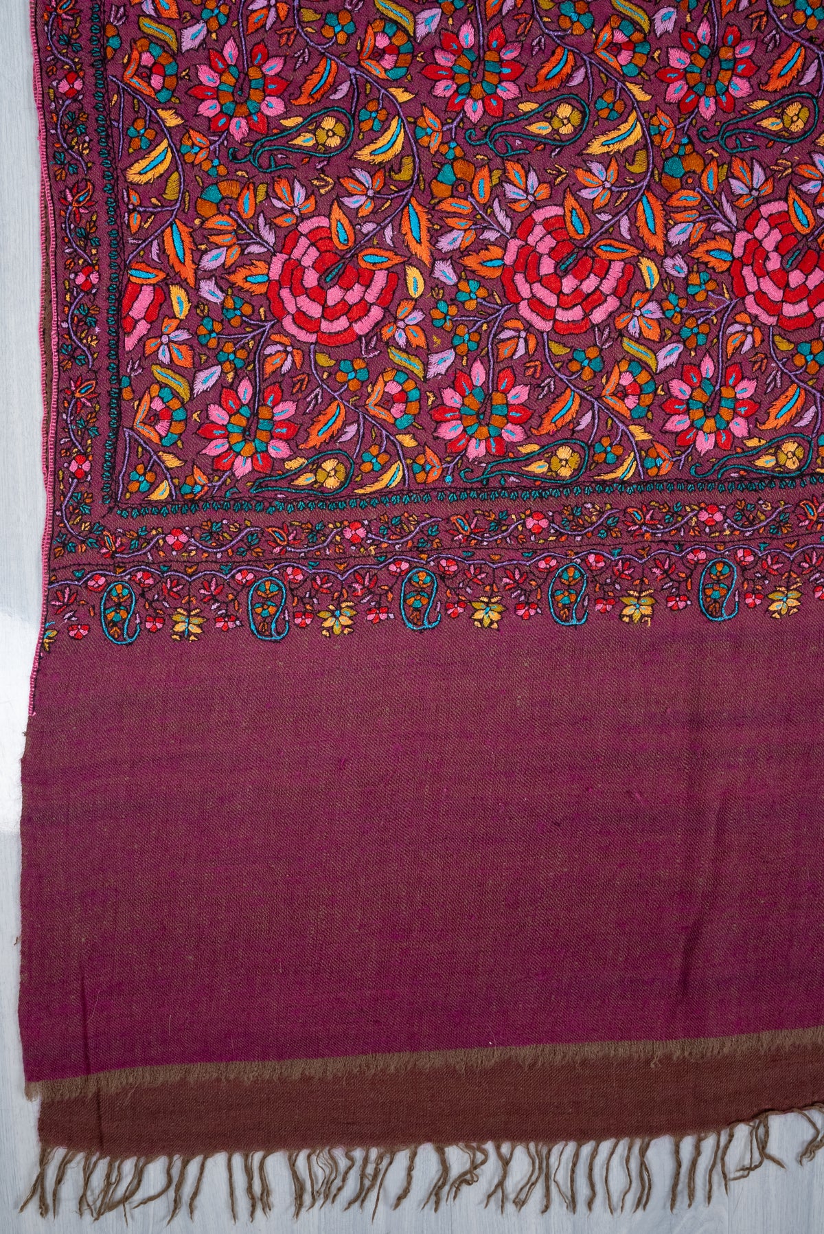 Corner of a plum Pashmina shawl, with embroidered floral borders and small hanging paisleys above the plain fringed end