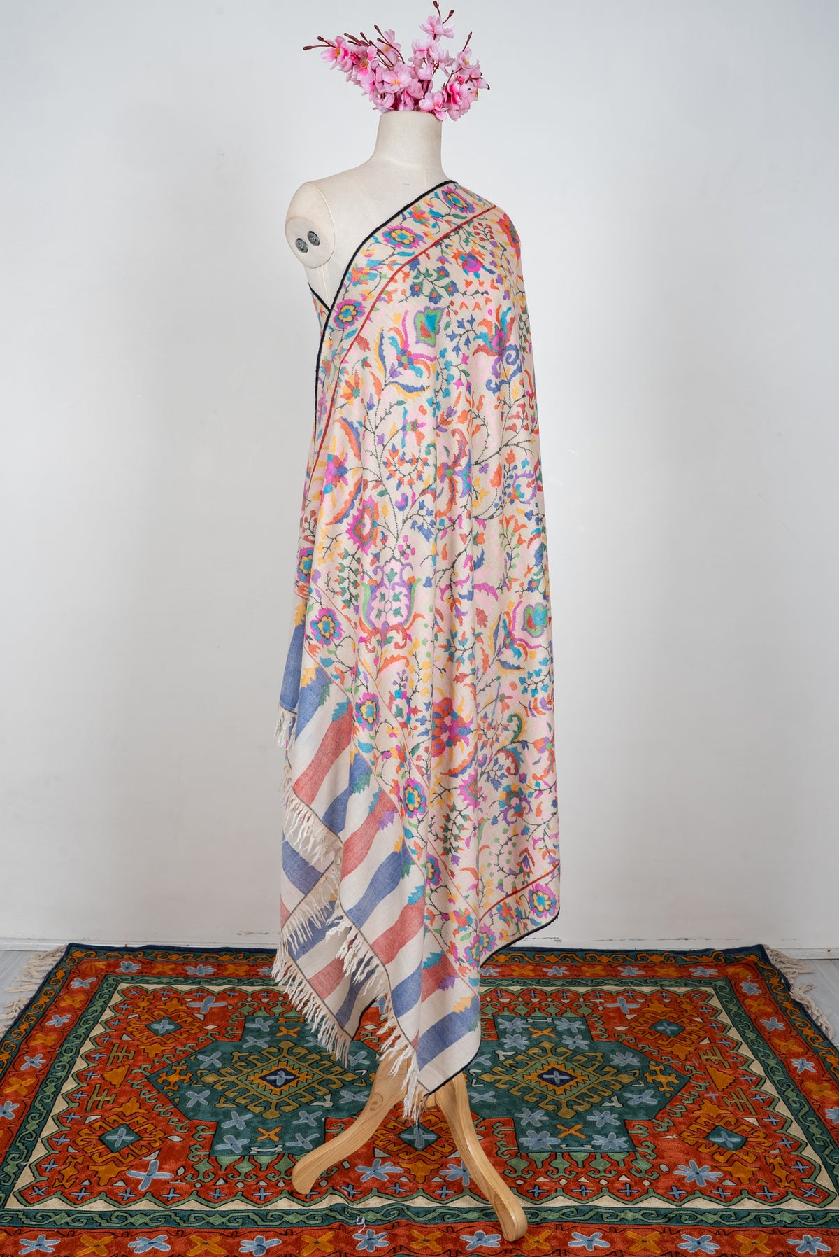 Full-length ivory Pashmina shawl draped on a mannequin, with colourful floral patterns and striped fringed ends
