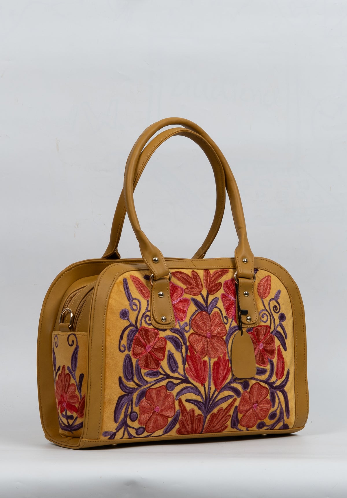 Opposite angled view of the mustard bag with upright handles, a hanging tag and red-orange flowers framed by purple vines.