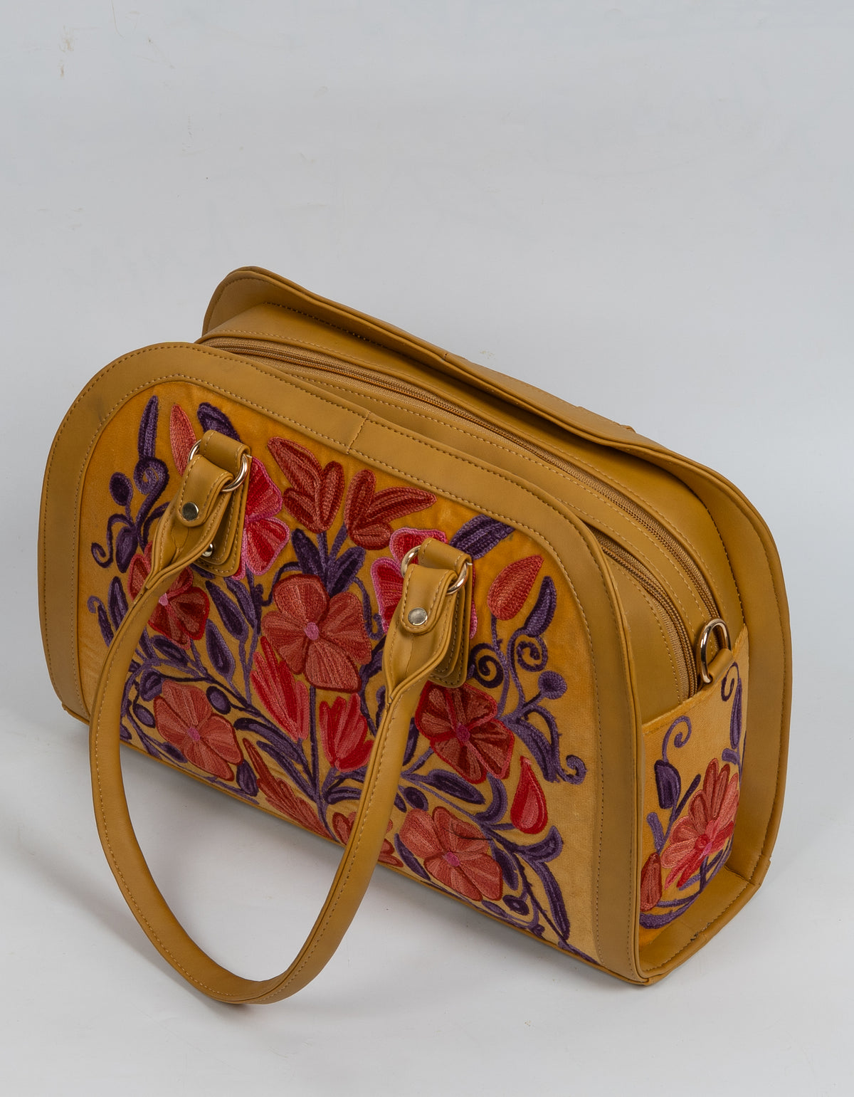 High angled view of the mustard bag with handles lowered, showing red-orange floral embroidery and the zipped top.