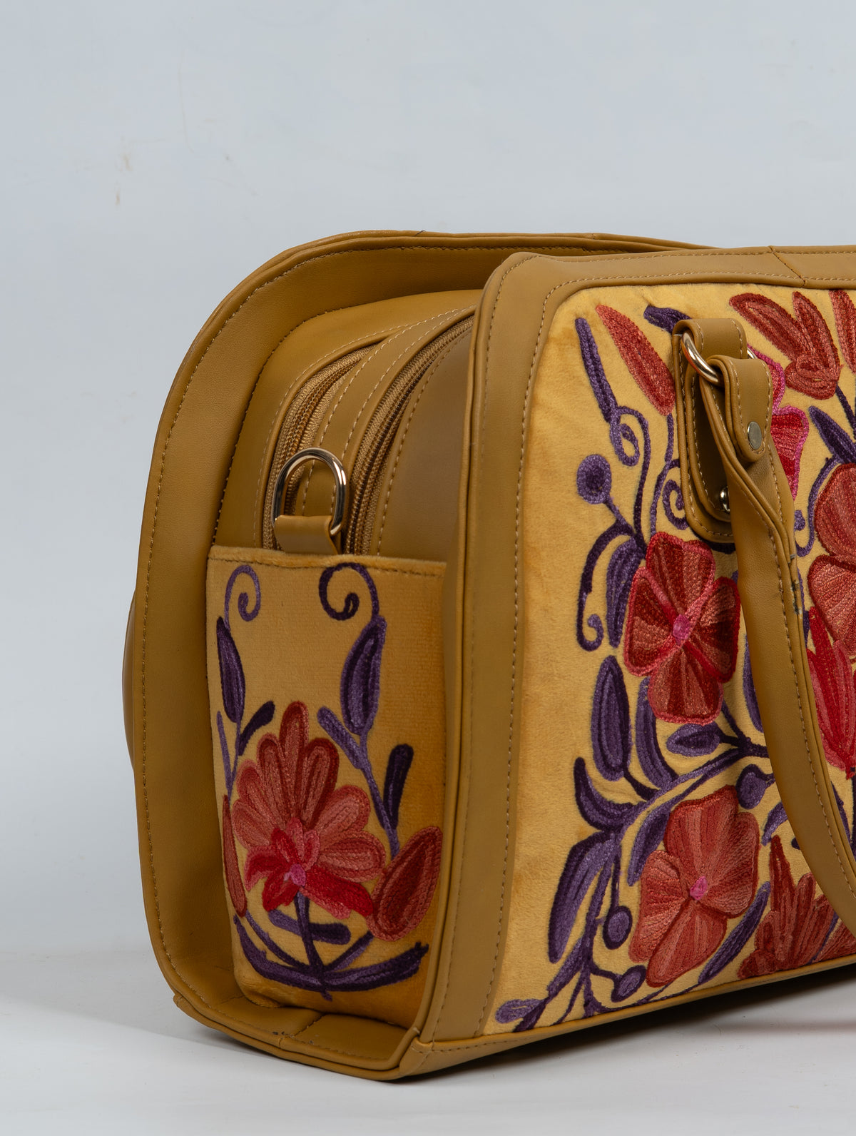 Close-up of the mustard bag’s side pocket, zipper ring and red flower embroidered among purple stems.