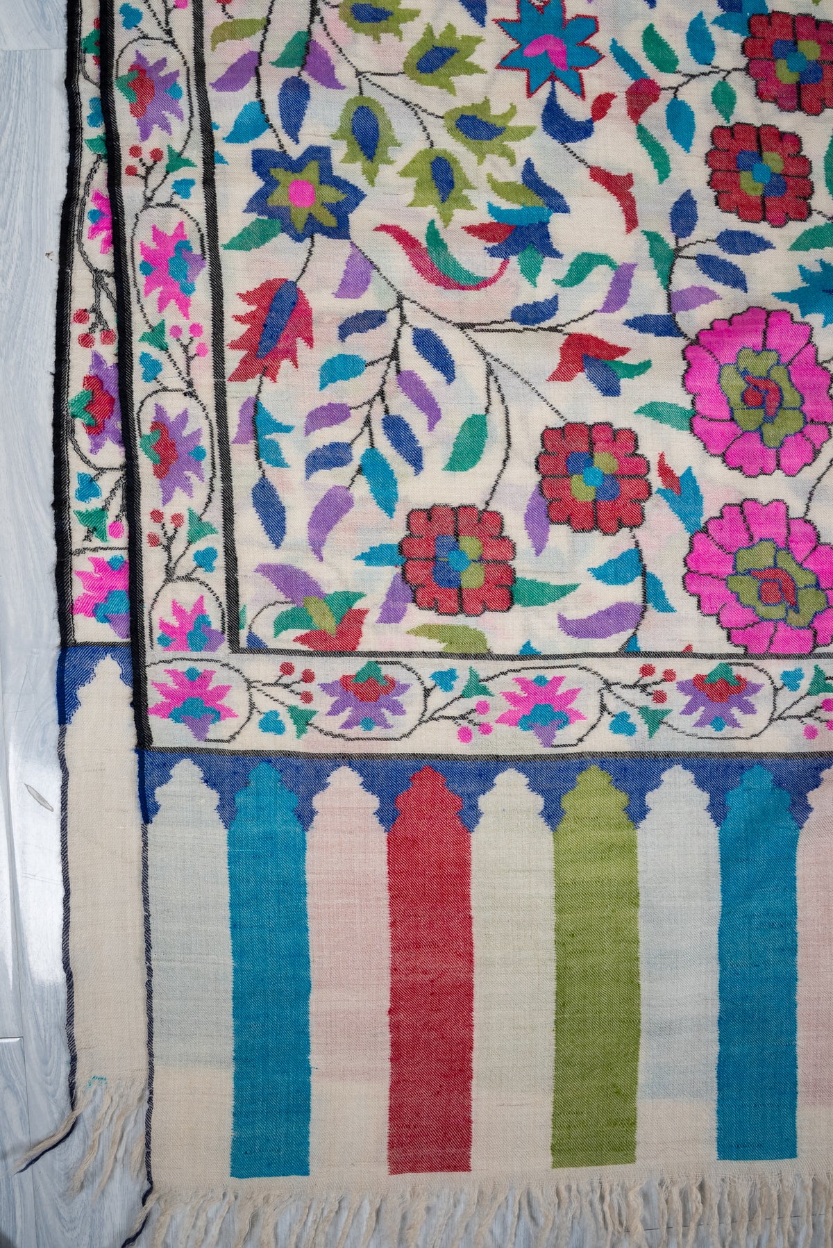 Corner of an ivory Pashmina shawl with pink flowers above turquoise, red and green end panels and cream fringe