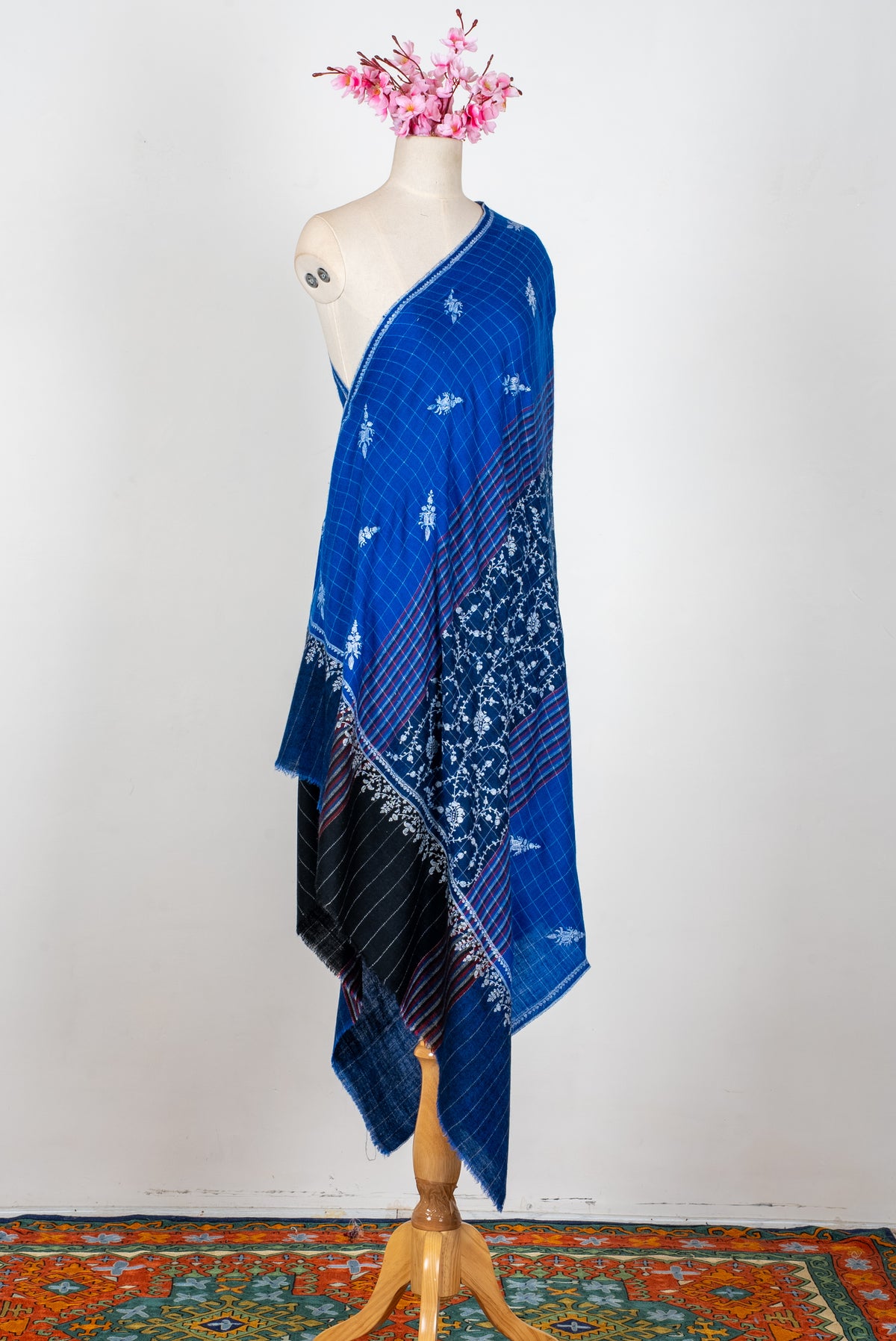 Full-length royal-blue Pashmina shawl draped on a mannequin, with white floral embroidery, checked panels and a dark end