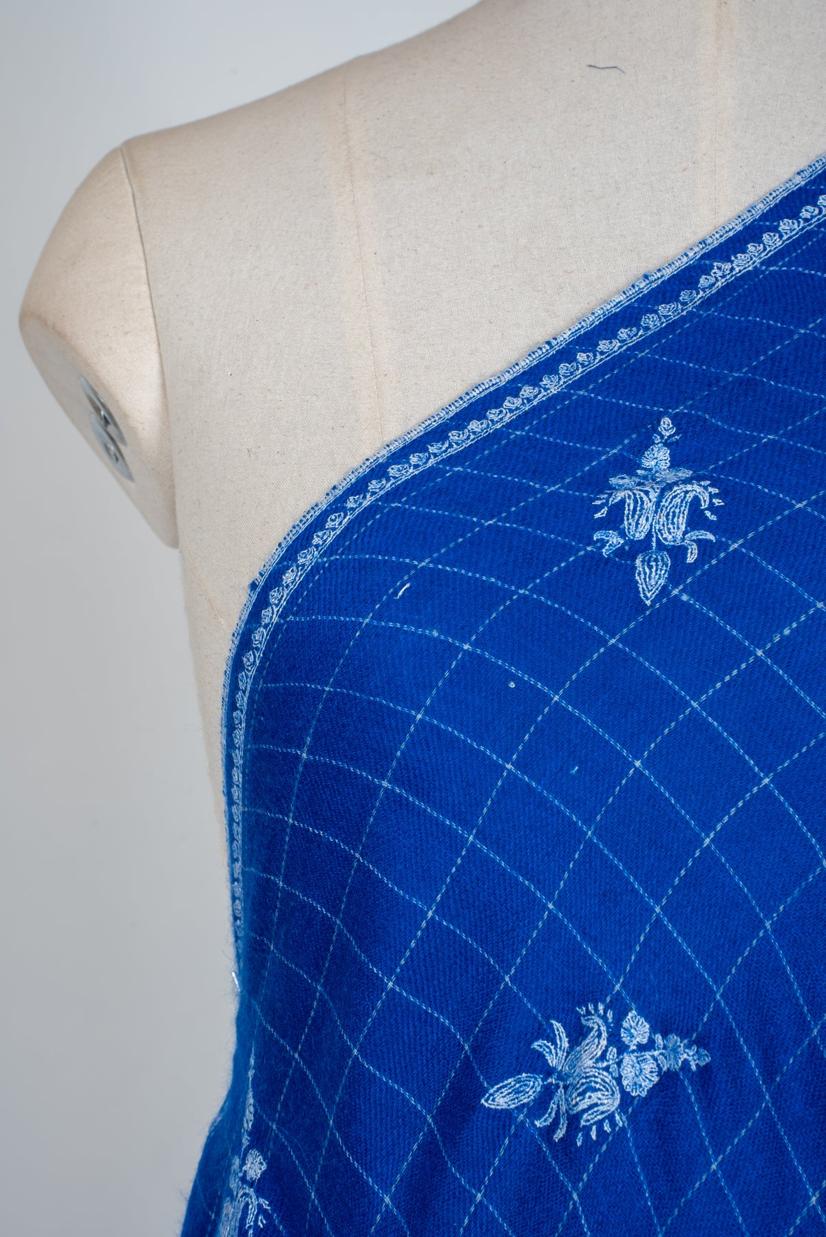 Shoulder close-up of royal-blue Pashmina shawl with white floral sprigs, fine checks and a narrow embroidered border