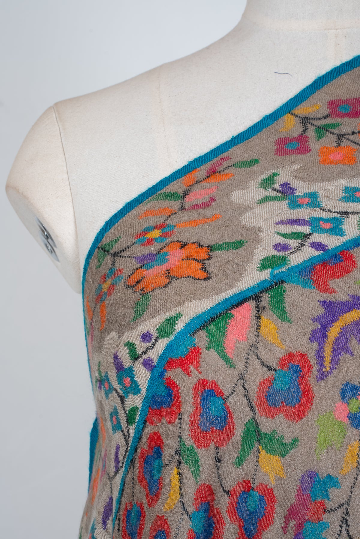 Shoulder close-up of taupe Pashmina shawl showing colourful floral motifs and a broad border edged in turquoise