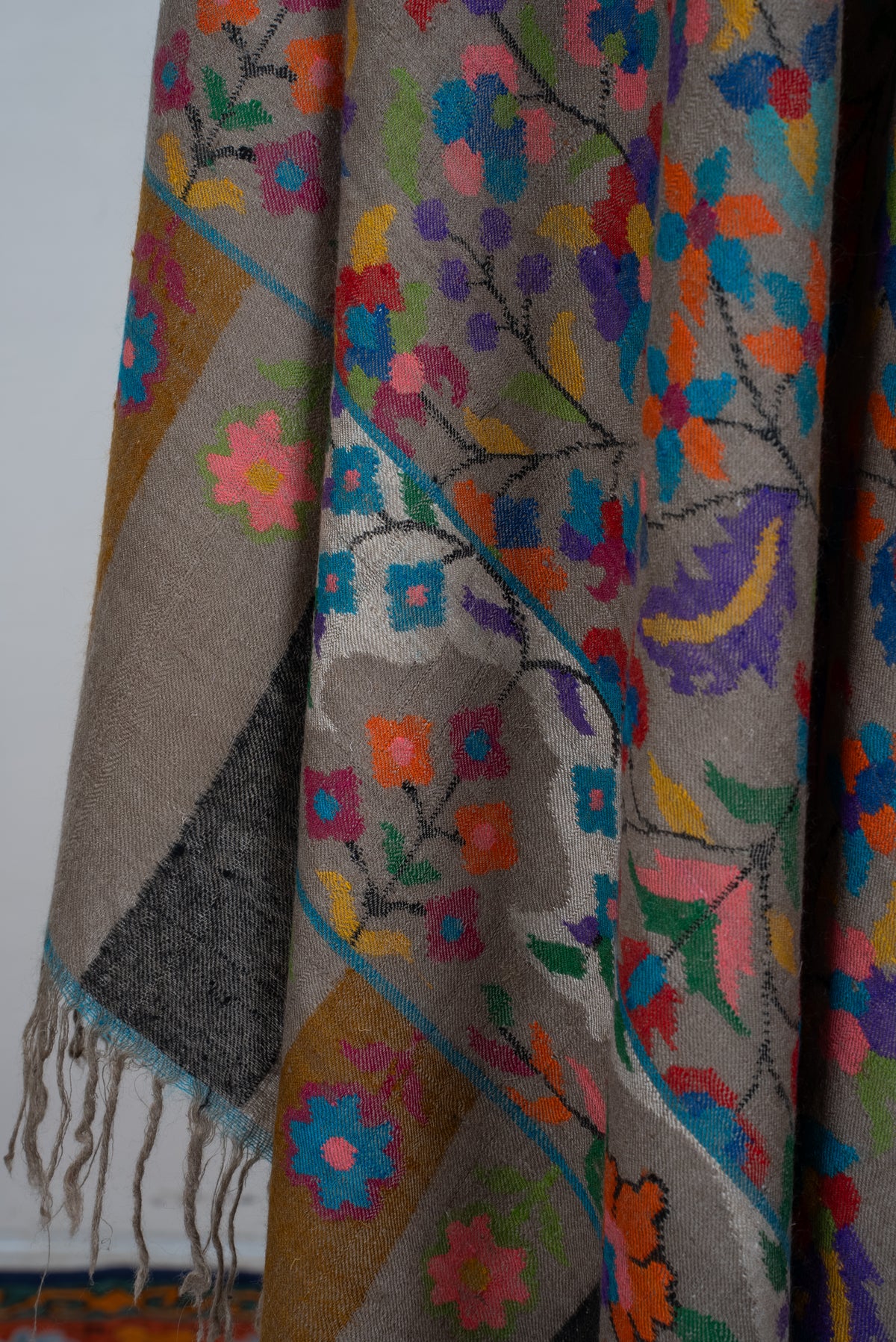 Close-up of Pashmina shawl folds with colourful flowers, a turquoise-edged border, striped end panels and fringe