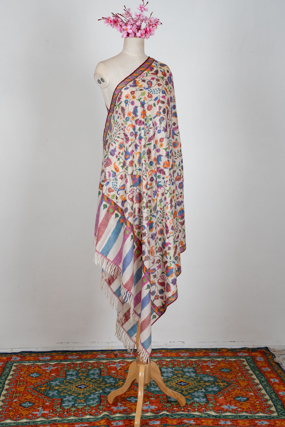 Ivory Pashmina shawl draped on a mannequin, covered in colourful floral vines with pastel striped ends and ivory fringe.