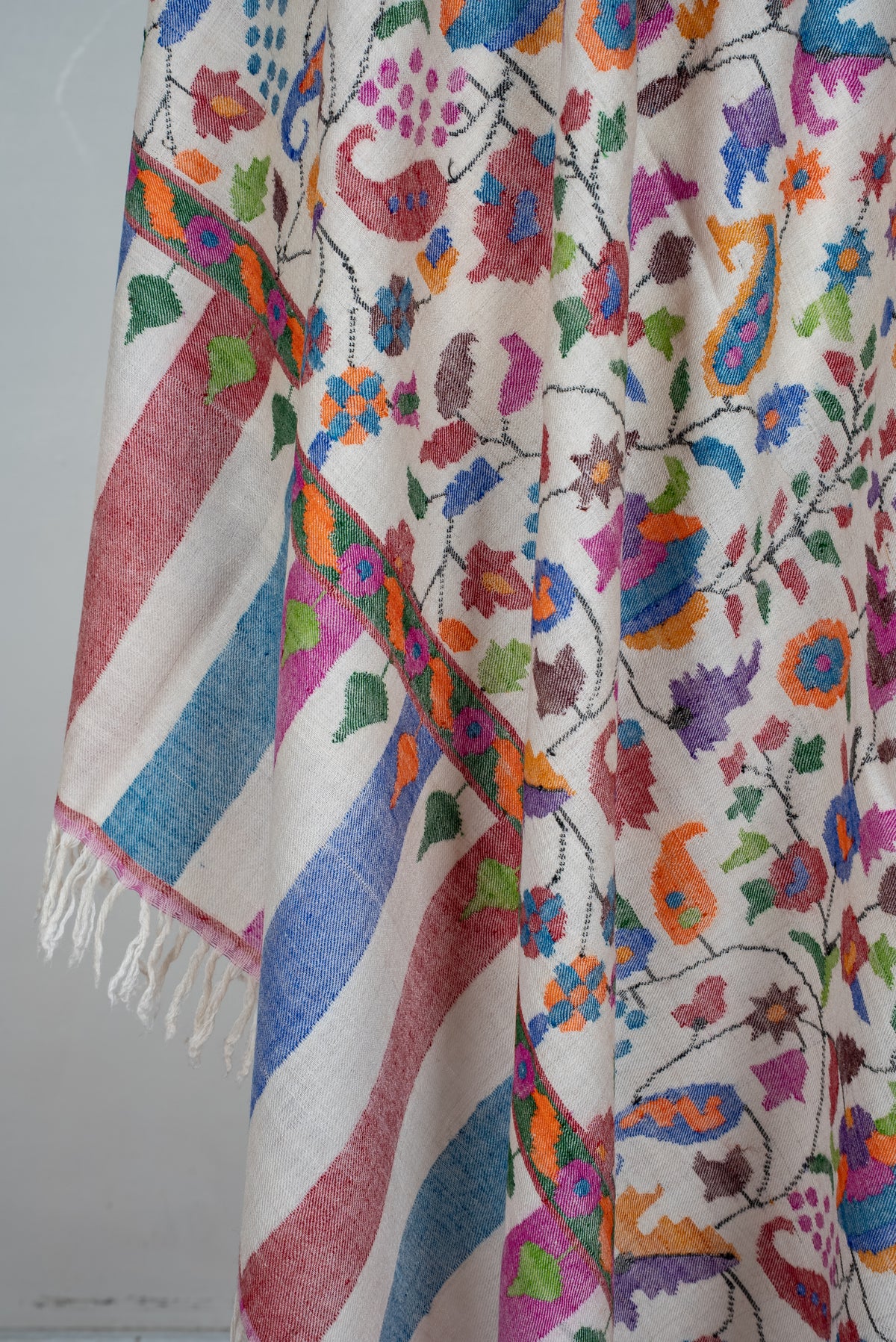 Draped ivory Pashmina shawl end, with multicoloured floral motifs, pink and blue stripes and ivory fringe.