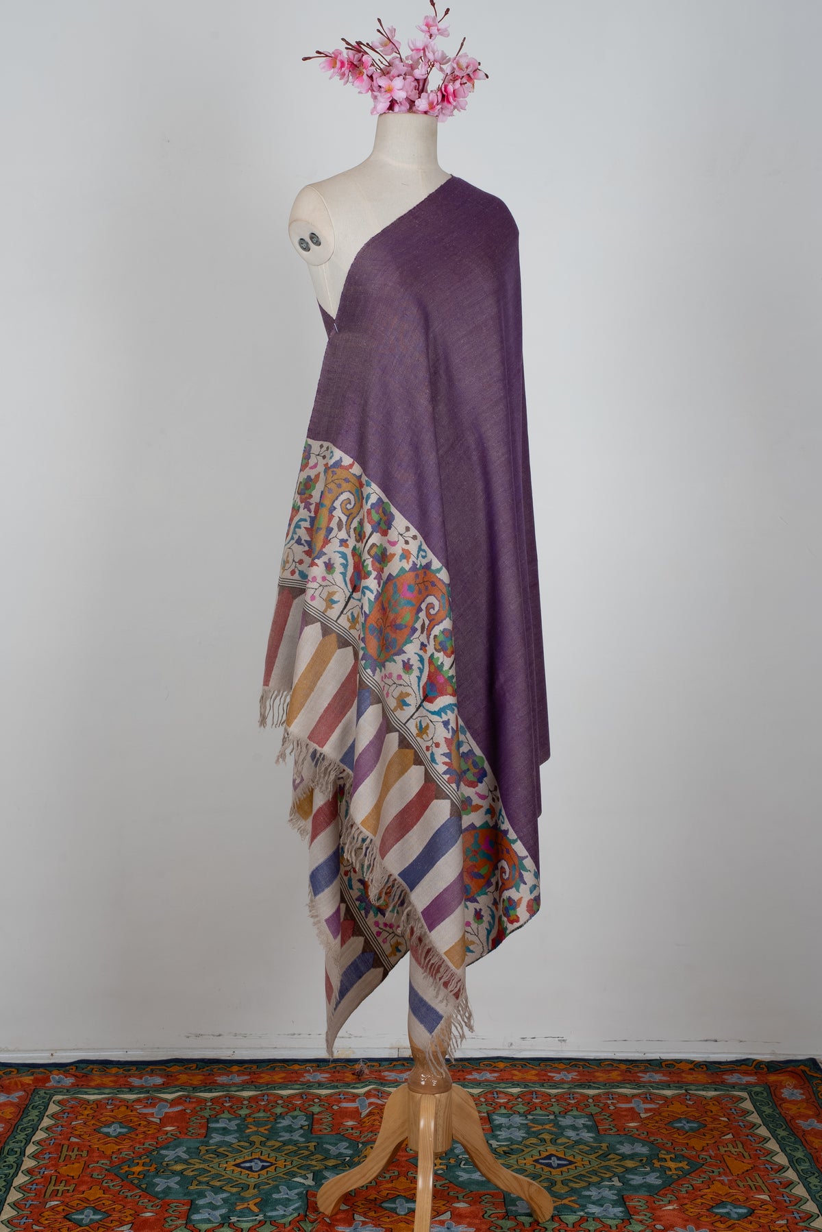 Purple Pashmina shawl draped on a mannequin, with a colourful paisley-and-flower end panel, striped tips and ivory fringe.