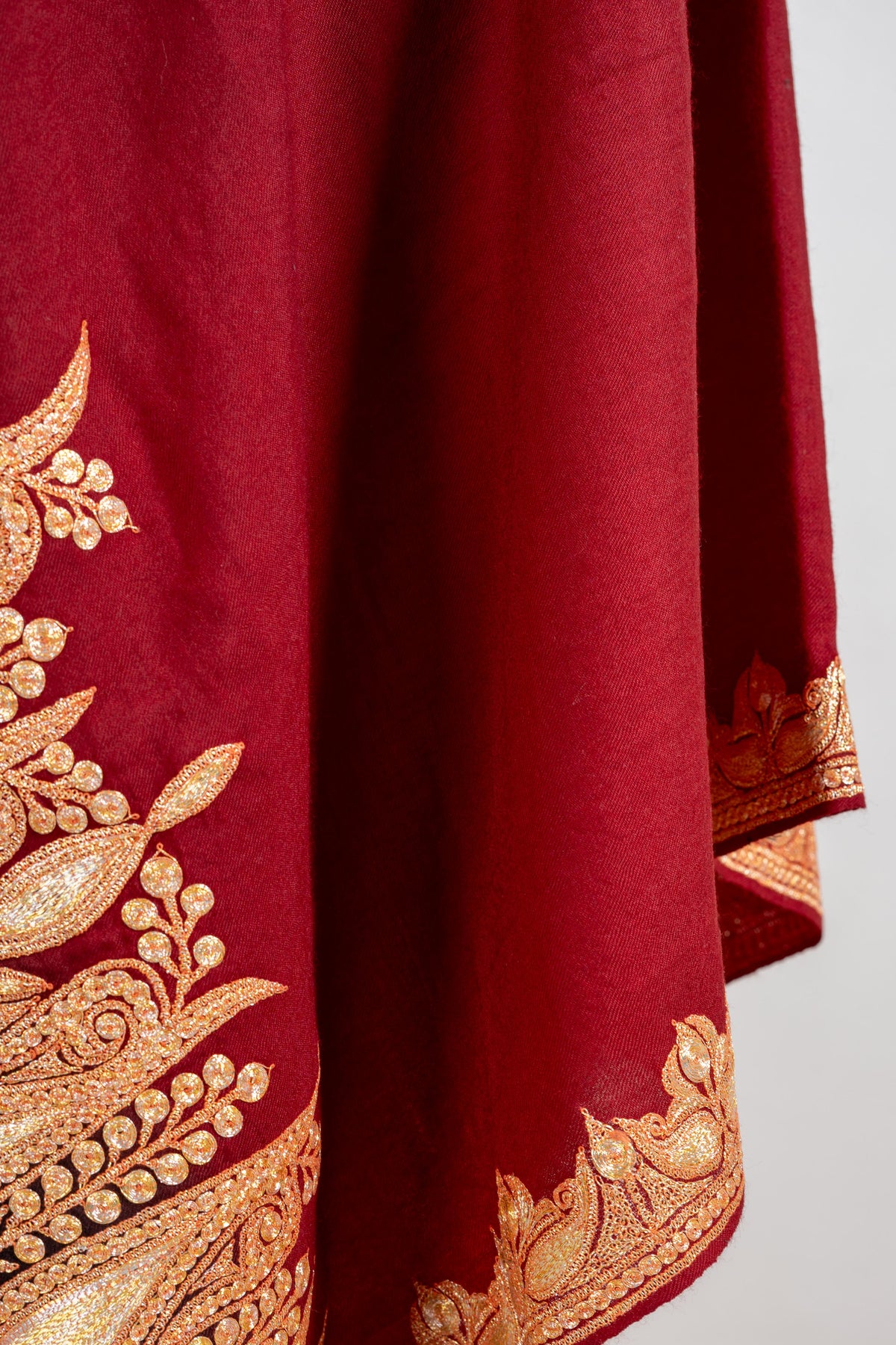 Draped crimson shawl folds showing the broad gold-coloured embroidered end band and narrower side edging.