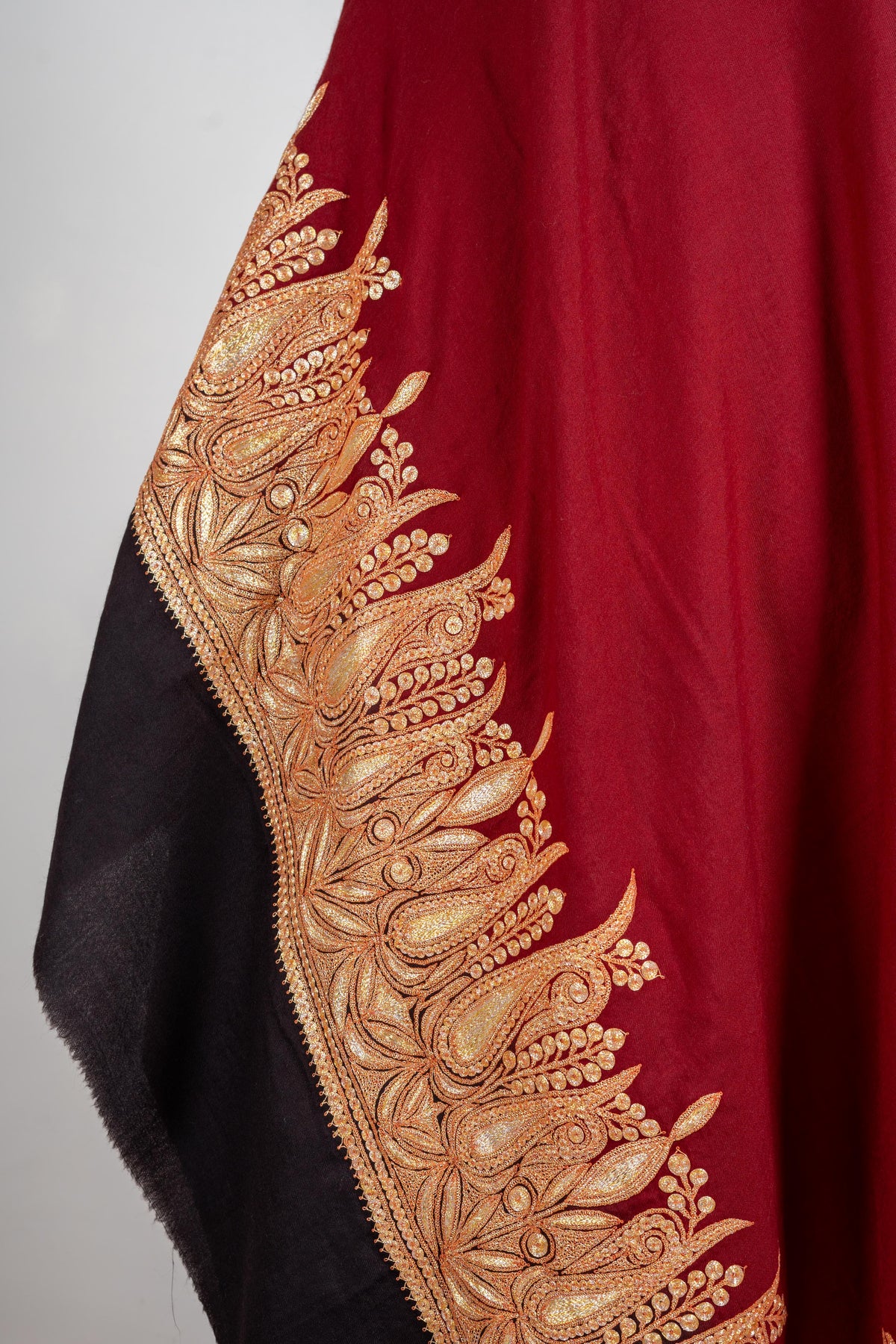 Hanging shawl detail showing a broad gold-coloured paisley, leaf and bud border between crimson and black fabric.