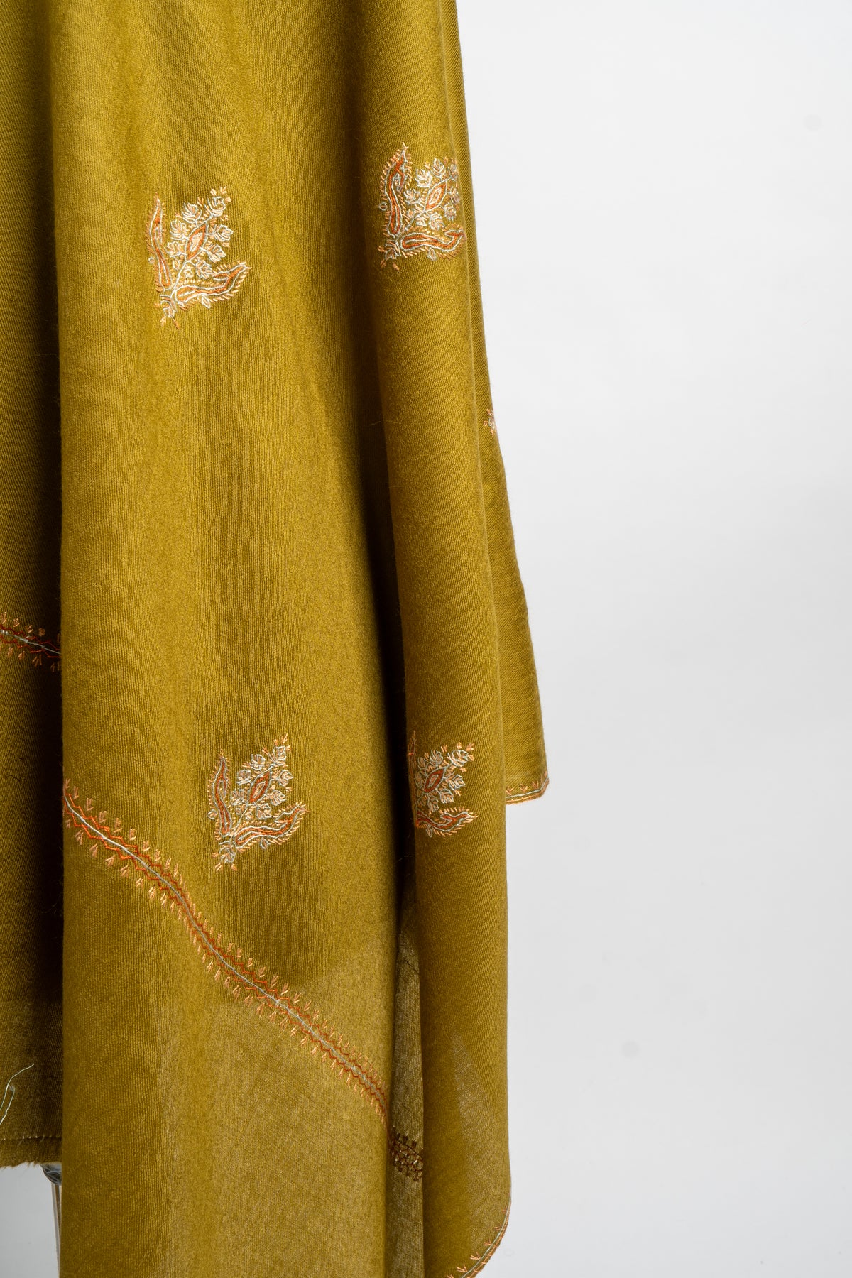 Detail of the olive-green stole’s hanging folds, with pale floral sprigs and a fine peach-toned border.