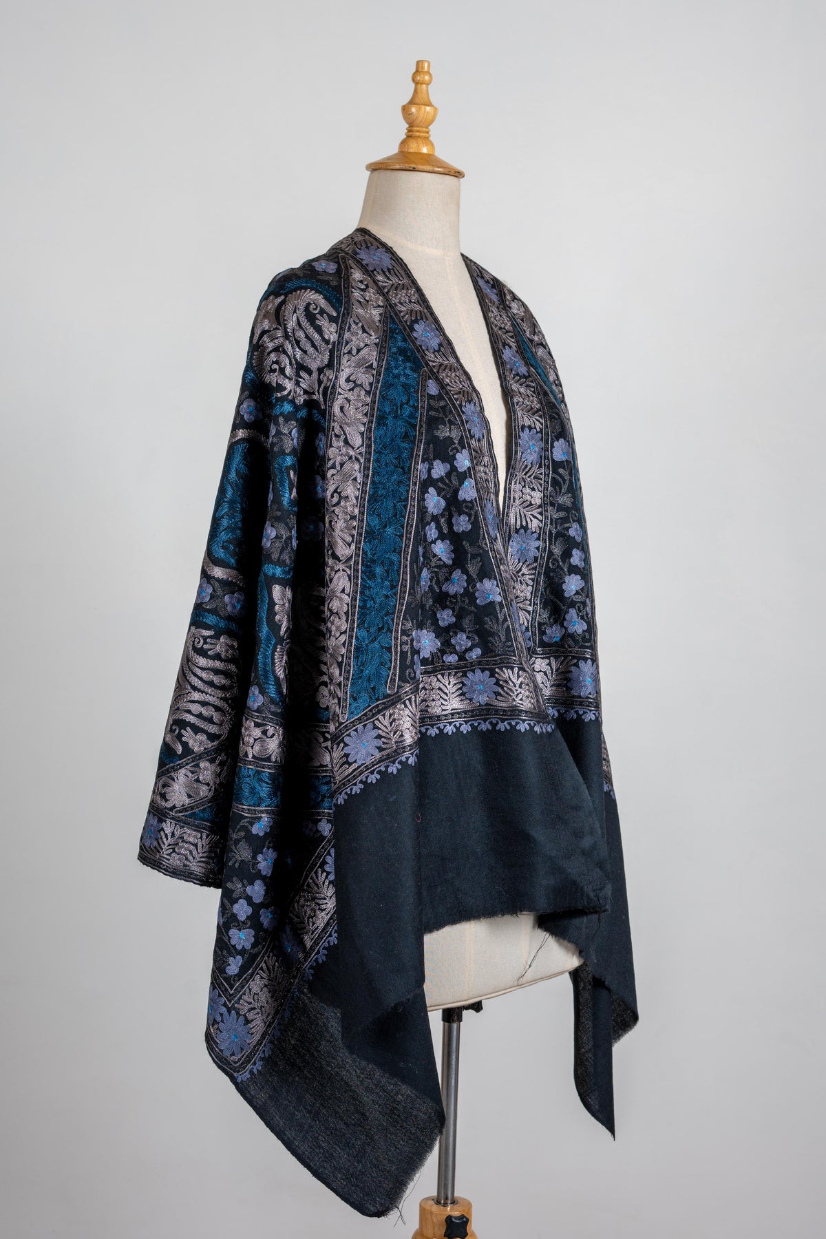 Black stole draped open over a mannequin’s shoulders with blue floral panels, silver-toned borders and plain ends