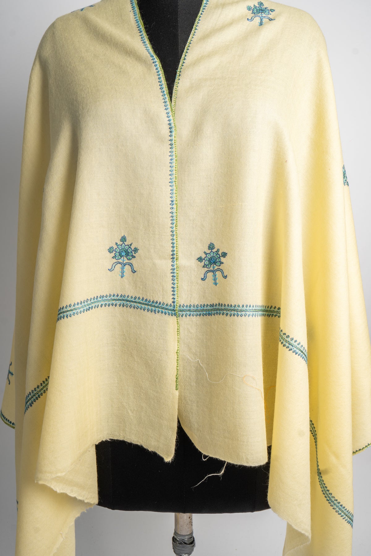 Front detail of the buttercream stole on a mannequin, showing paired teal floral motifs and narrow borders above the fringed ends.