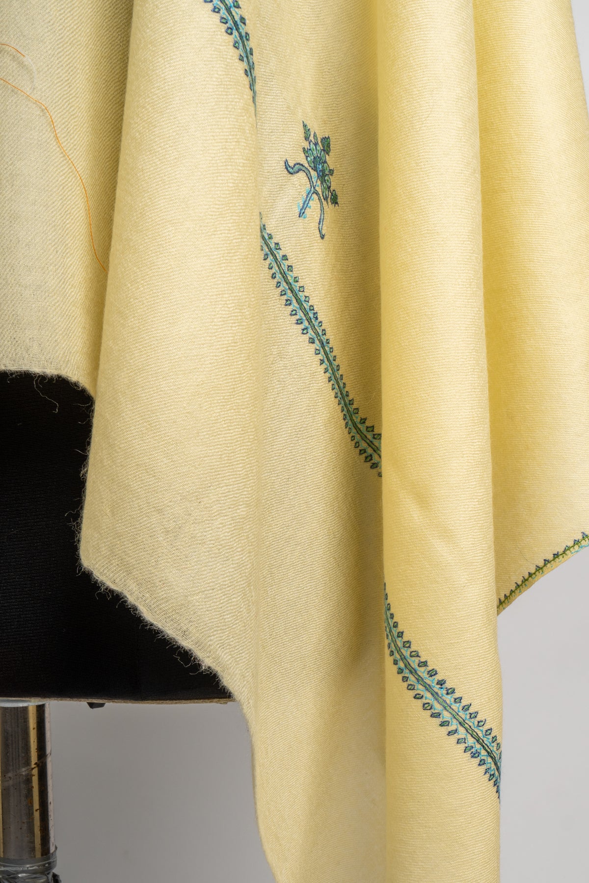 Close-up of the buttercream stole’s hanging end, showing a narrow teal embroidered border and fine fringe.