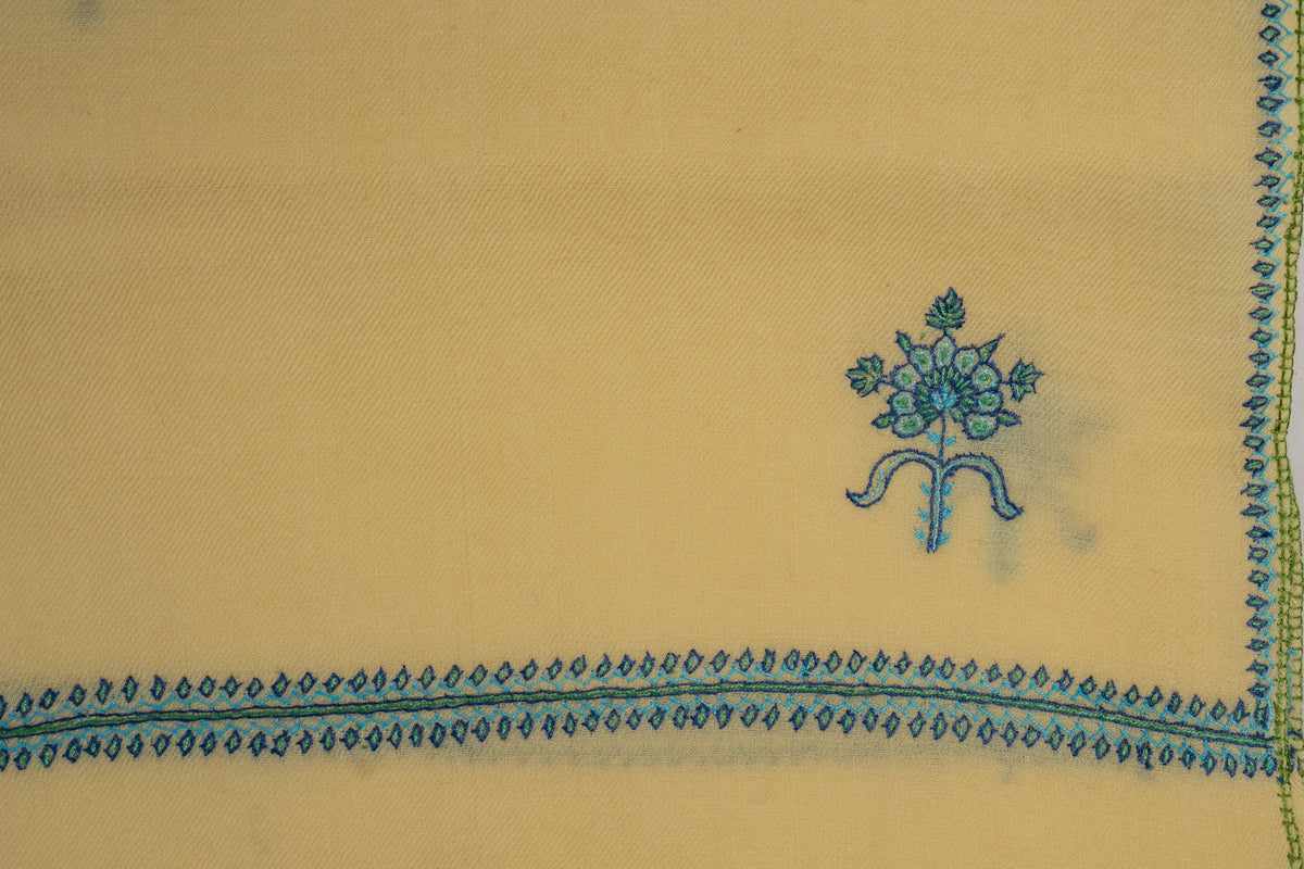 Flat corner detail of the buttercream stole, with a teal floral motif above intersecting leaf-pattern borders.