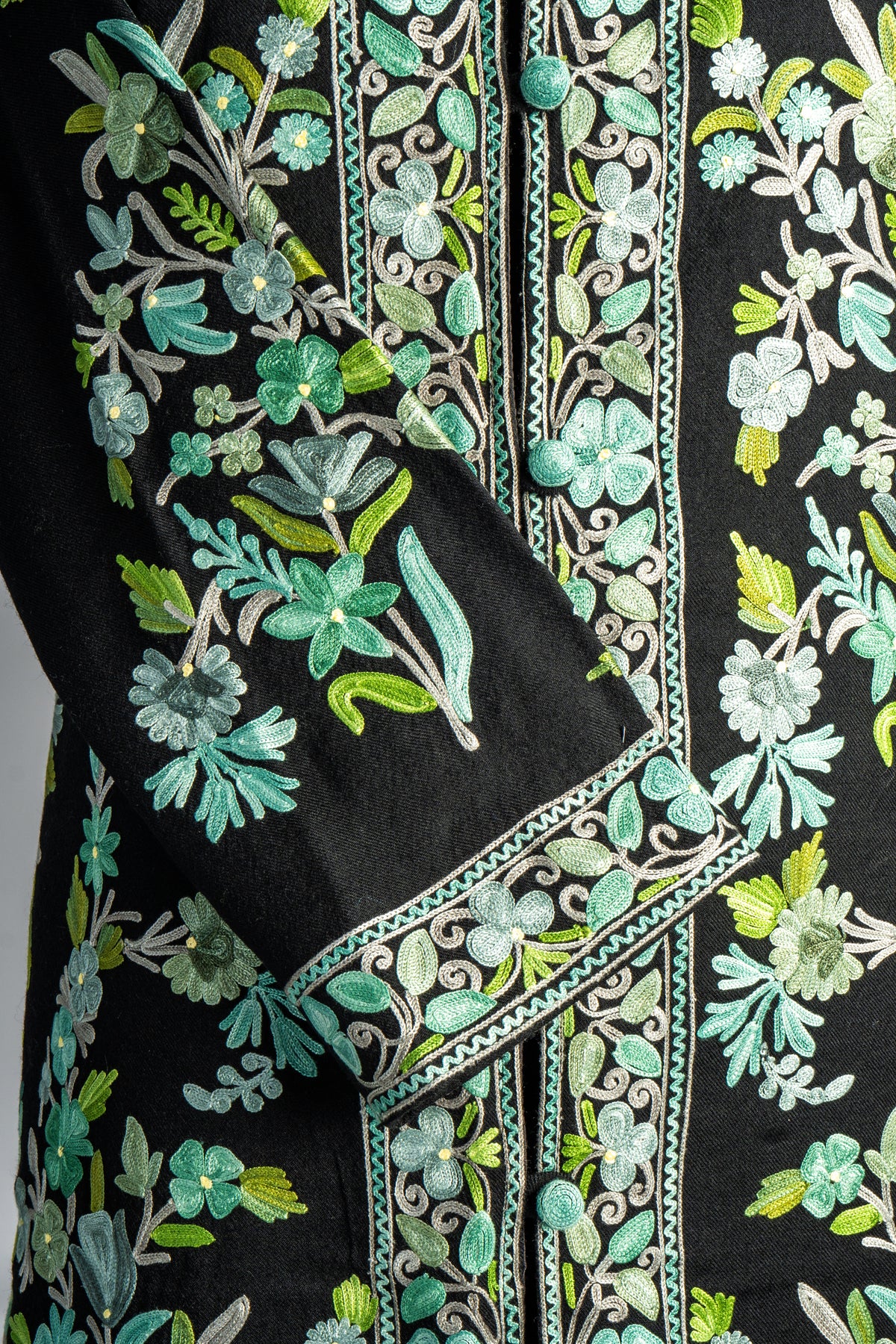 Close-up of mint and green Aari flowers on the black jacket’s folded sleeve beside the ornate front borders.