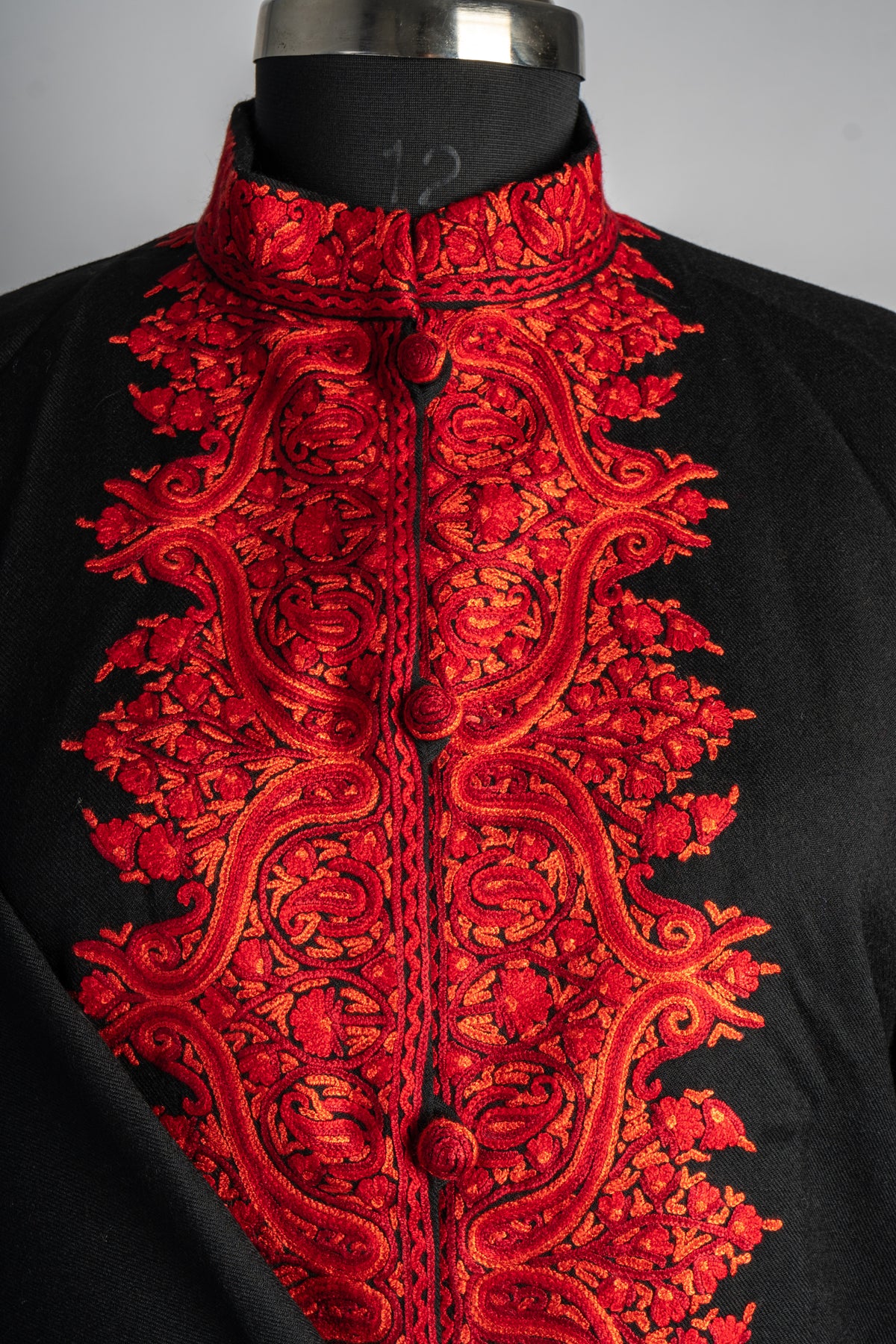 Black jacket neckline and chest with dense red and orange Aari paisleys, covered buttons and an embroidered stand collar