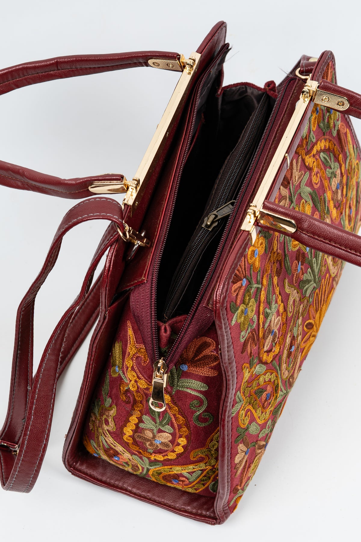 Close-up of the open top of a maroon embroidered handbag with a dark lining, zip closure and gold-toned frame fittings