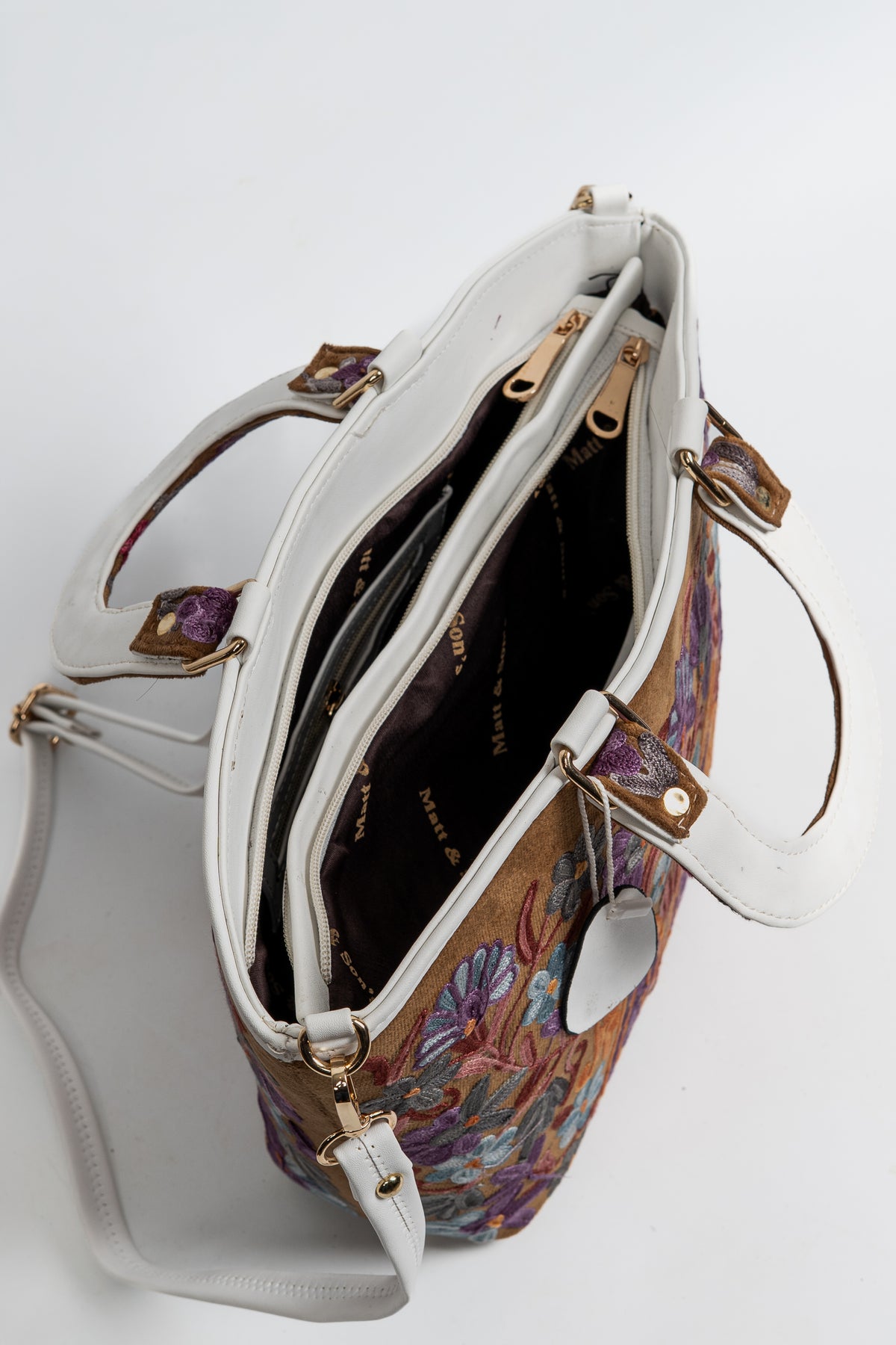 Top view of the open brown floral tote showing its dark lining, internal zipped divider and white trim and shoulder strap.