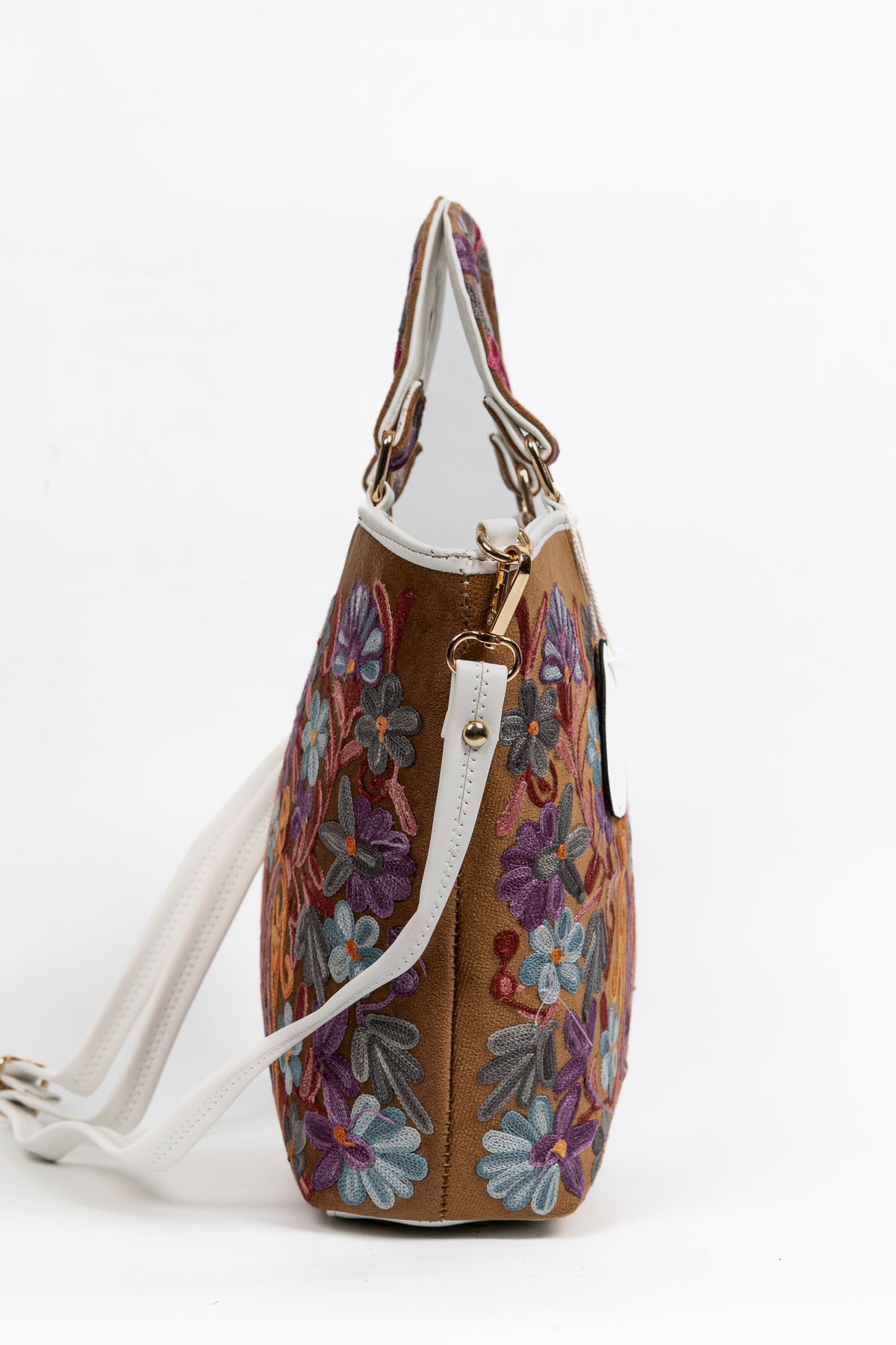 Side view of the tapered brown tote with floral embroidery, white edging and a detachable white shoulder strap.
