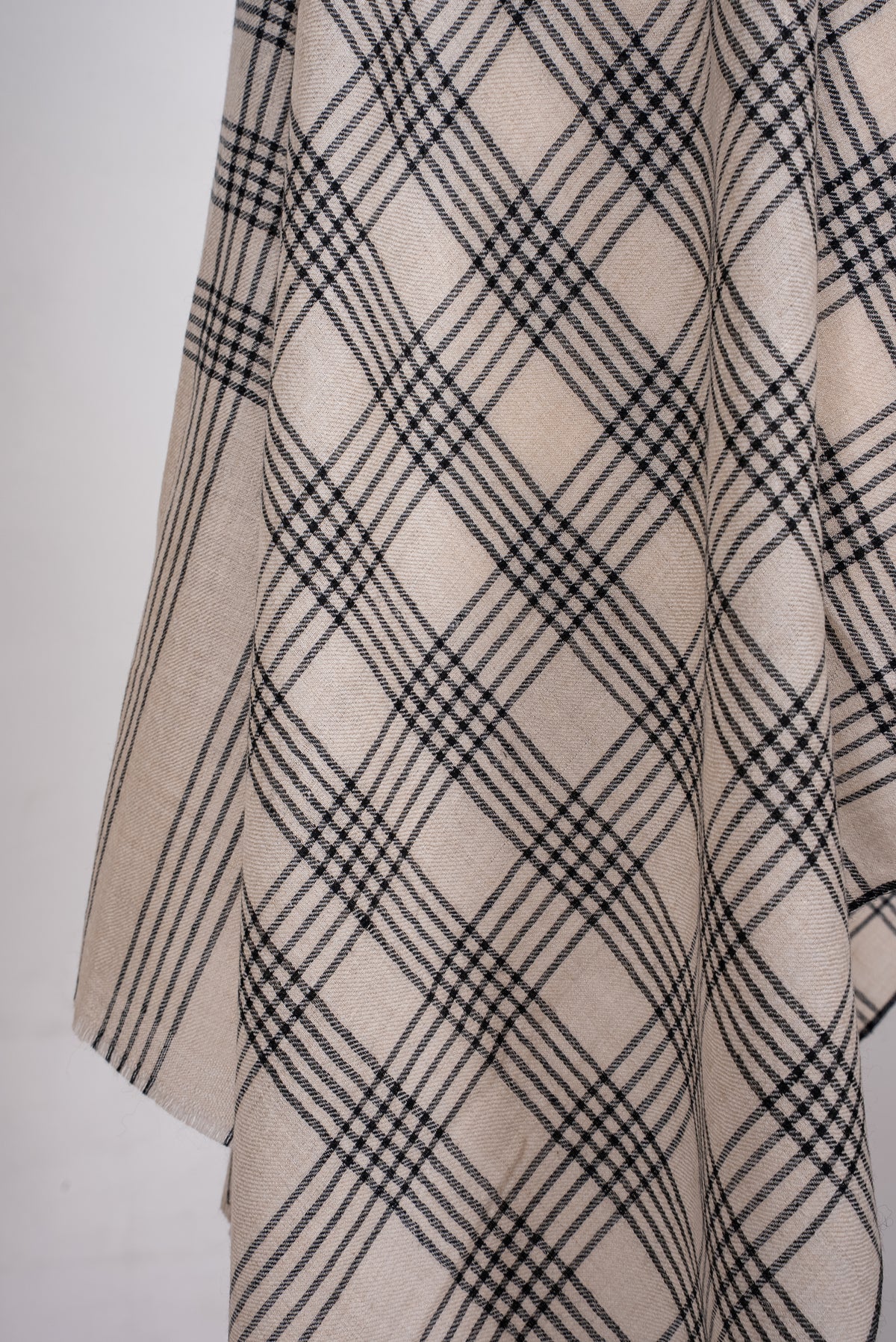 Close-up of hanging ivory Pashmina scarf folds, showing black plaid checks and the striped end panel