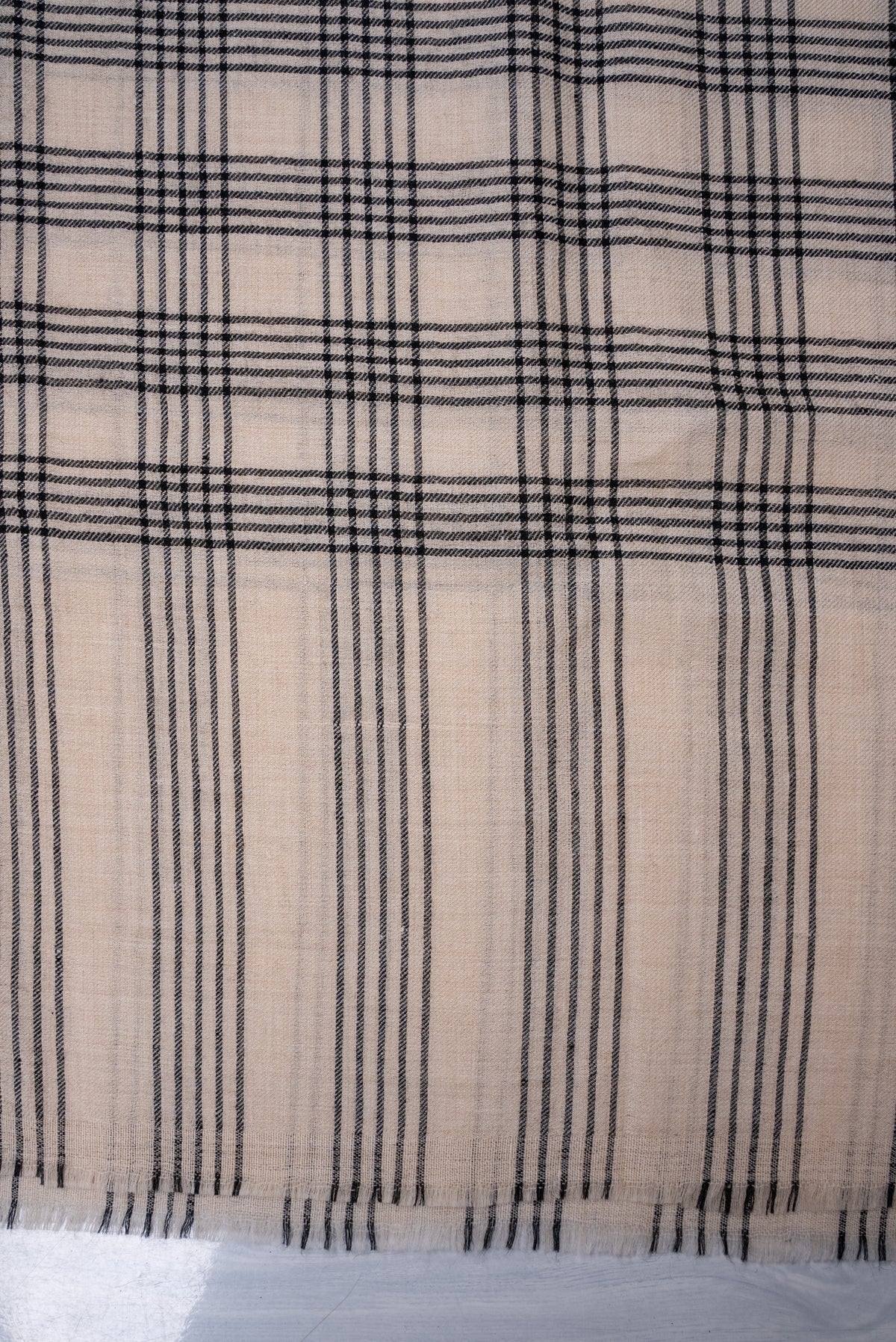 Close-up of the black striped end and short fringe beneath the plaid pattern on ivory Pashmina scarf