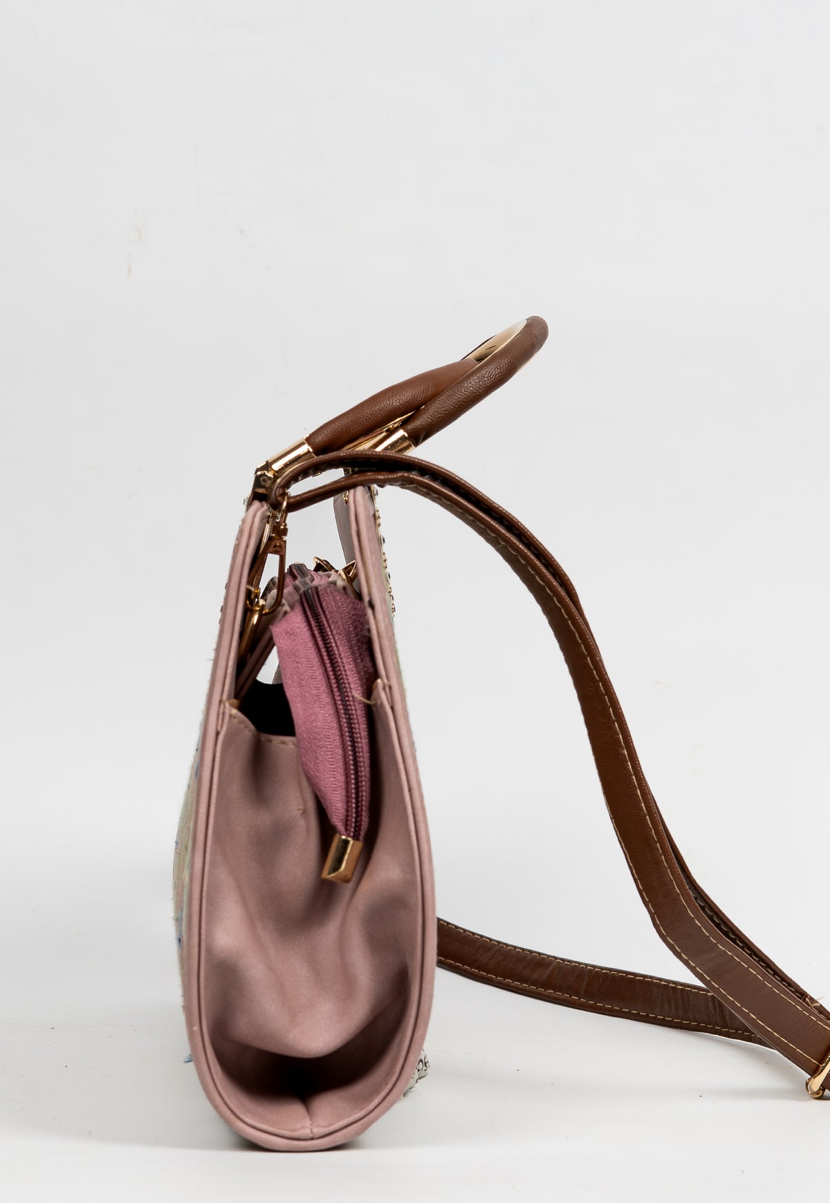 Side view of the mauve handbag, showing its gathered side, top zip and attached brown shoulder strap