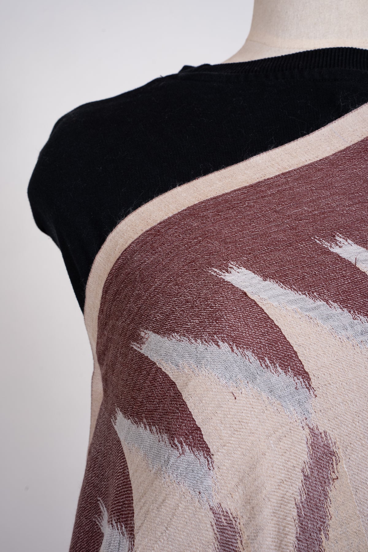 Shoulder close-up of the Merino wool scarf, showing beige, mocha and pale grey angular woven shapes and a narrow cream edge
