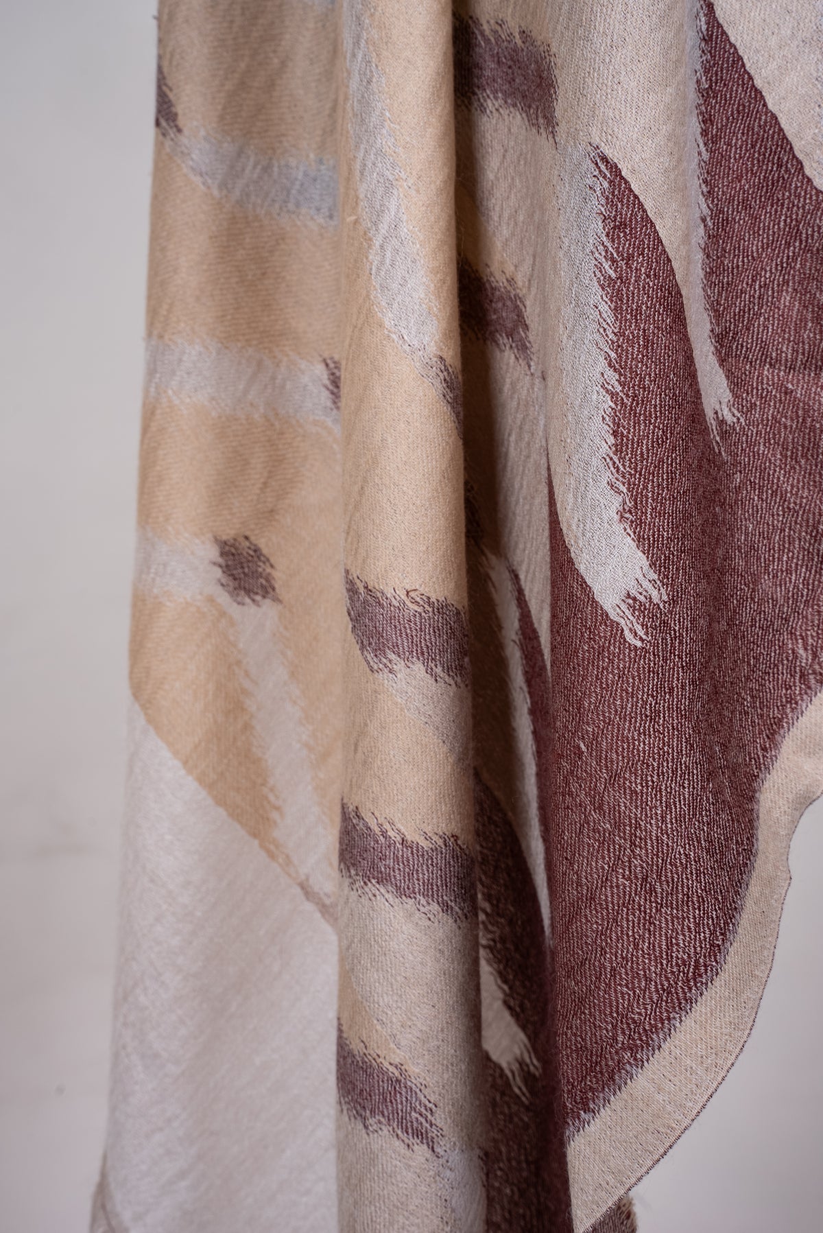 Lower draped detail of the Merino wool scarf, showing beige and mocha angular woven shapes and a pale end