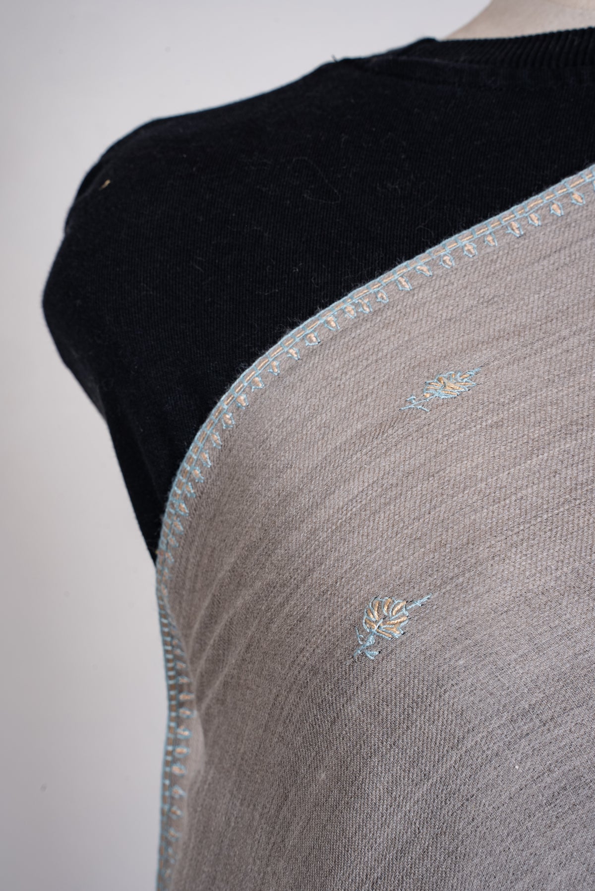 Shoulder close-up of dove-grey scarf showing small blue and beige leafy sprigs and delicate border embroidery