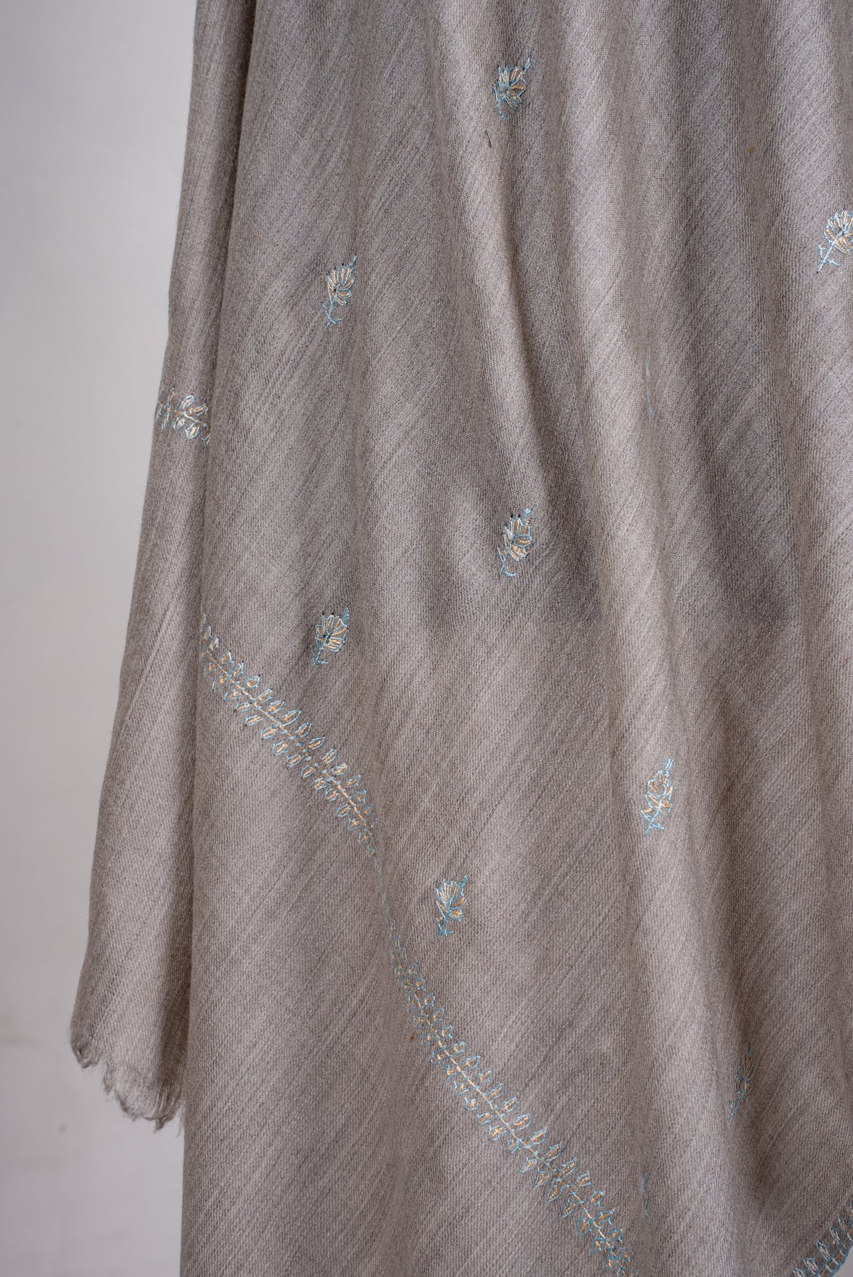 Close-up of dove-grey scarf folds showing tiny pale blue and beige embroidered sprigs and the matching end border