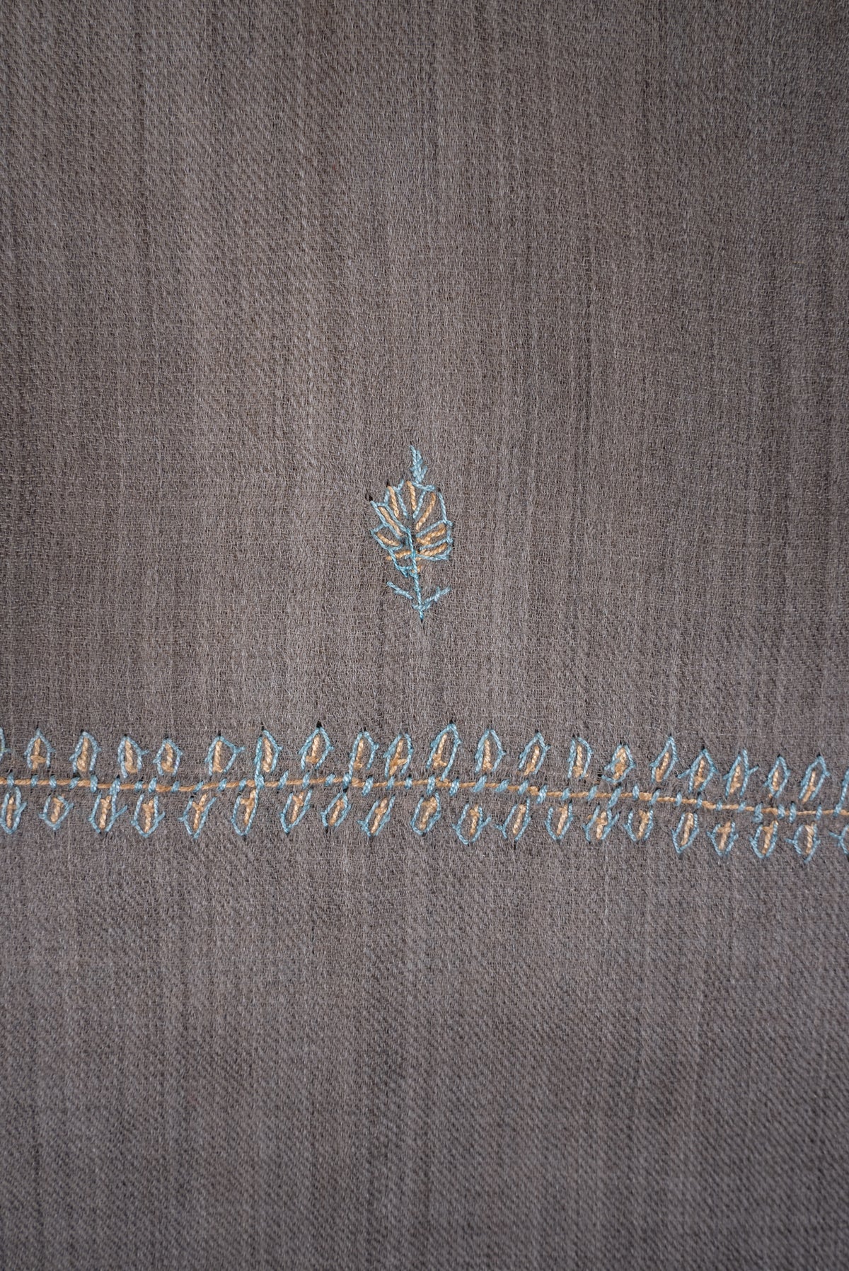 Detail of a pale blue and beige leafy sprig above the narrow embroidered border on dove-grey scarf