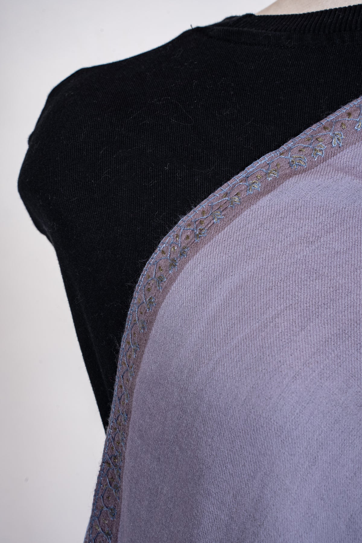 Close-up of a lavender scarf across a mannequin's chest, showing fine blue-and-olive floral embroidery along a darker edge band.
