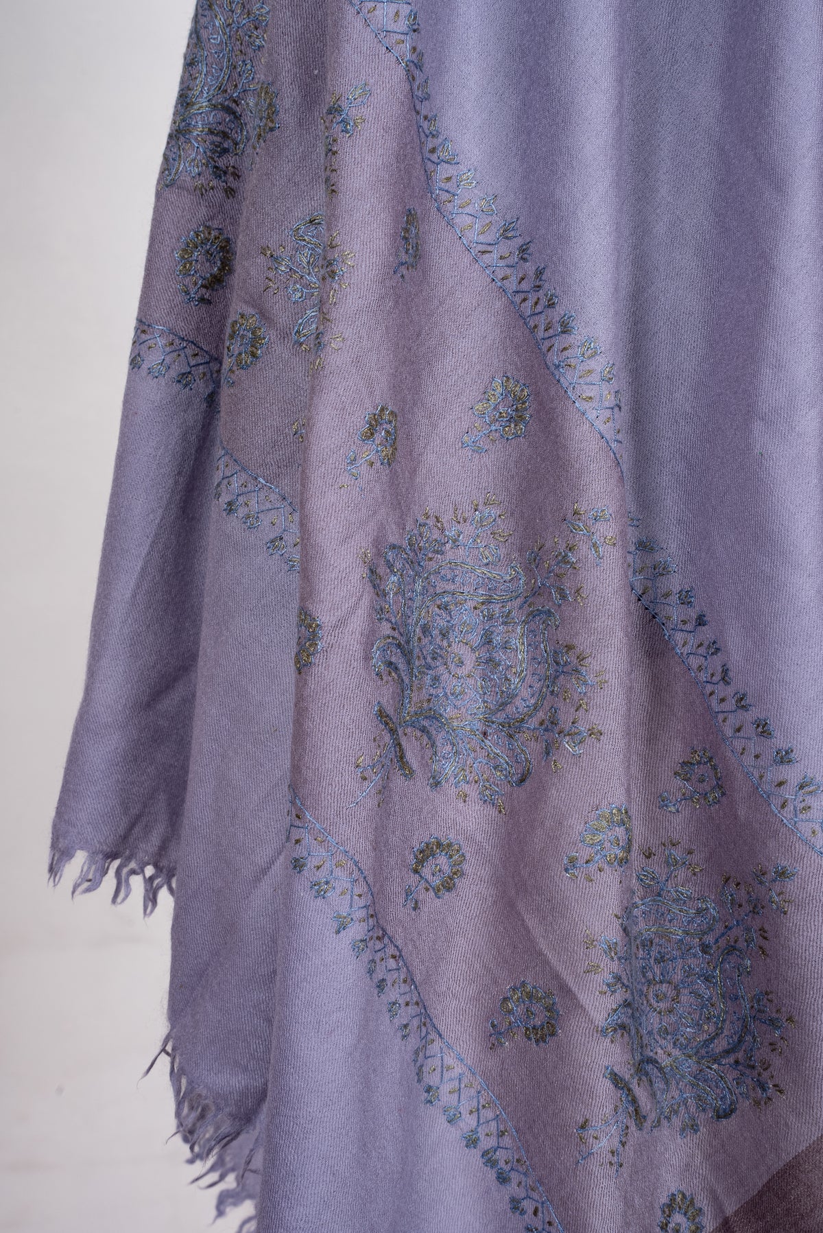 Detail of a draped lavender scarf end, with blue-and-olive embroidered floral bouquets and small sprigs in a darker mauve band.