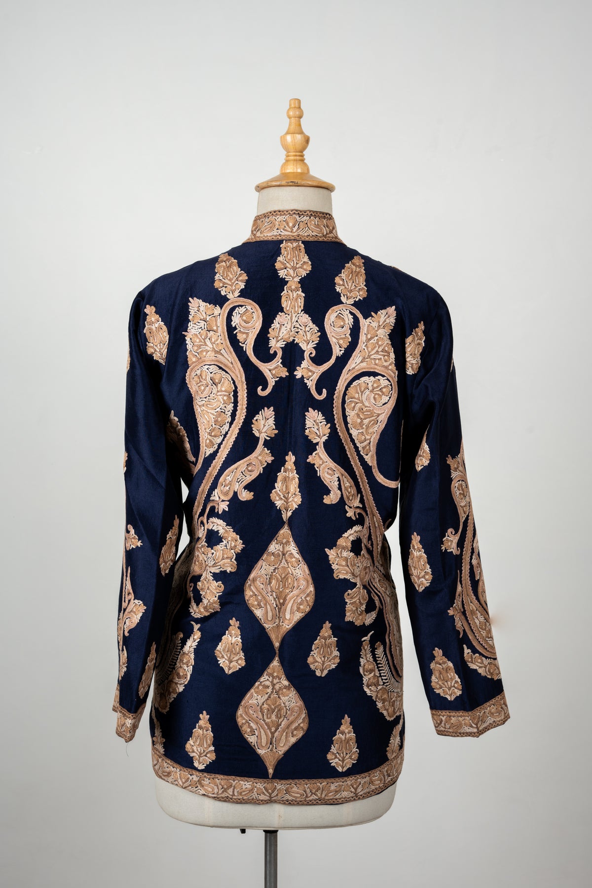 Rear view of a navy short jacket on a mannequin, with symmetrical beige Aari paisleys and scattered leaf motifs