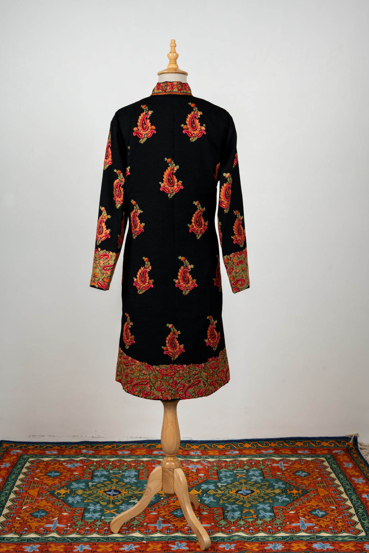 Full back of the black wool jacket with scattered red-and-orange paisley motifs and broad embroidered cuffs and hem.