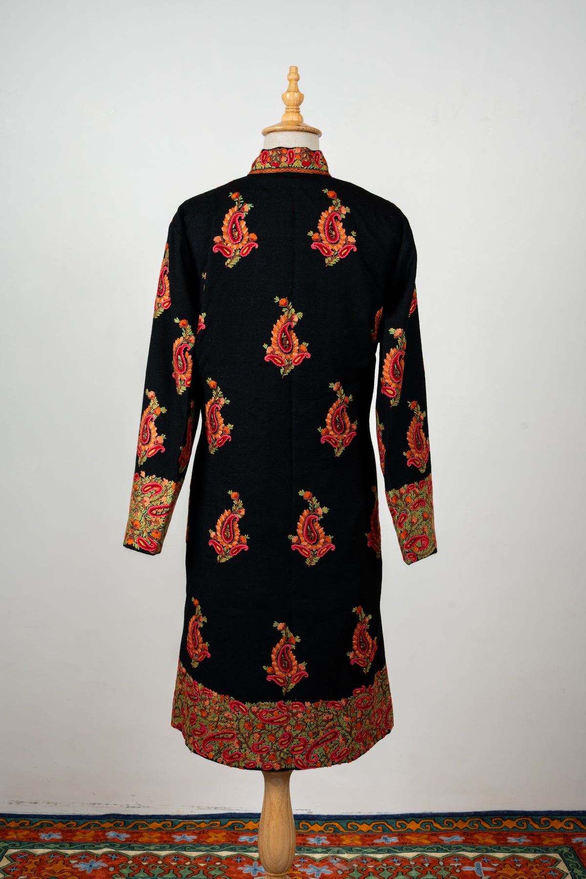 Closer rear view of the black jacket with spaced red paisleys, a floral stand collar and dense embroidery along the lower edge.