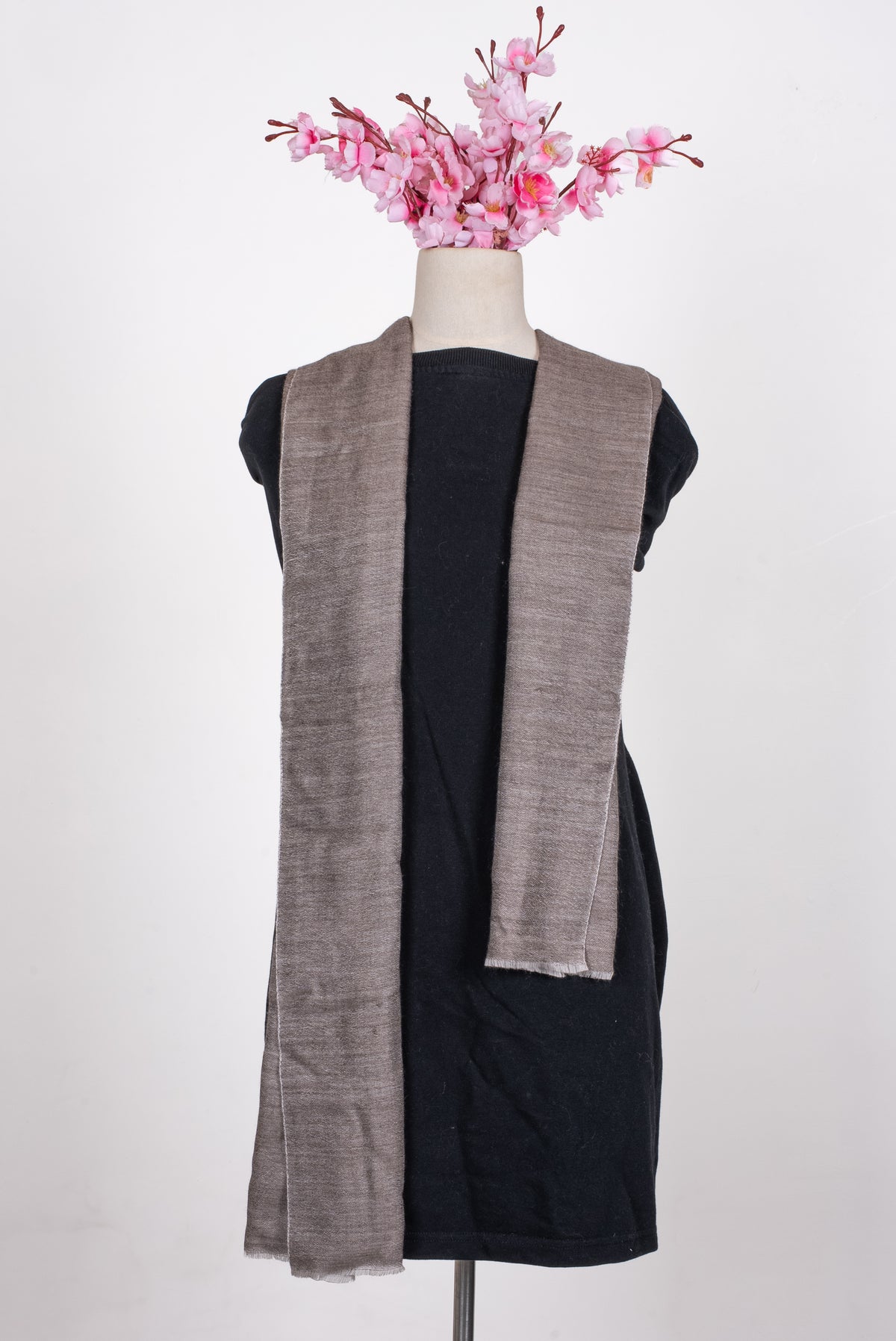 Taupe wool muffler draped open around a mannequin neck, with long uneven ends and pale short fringe