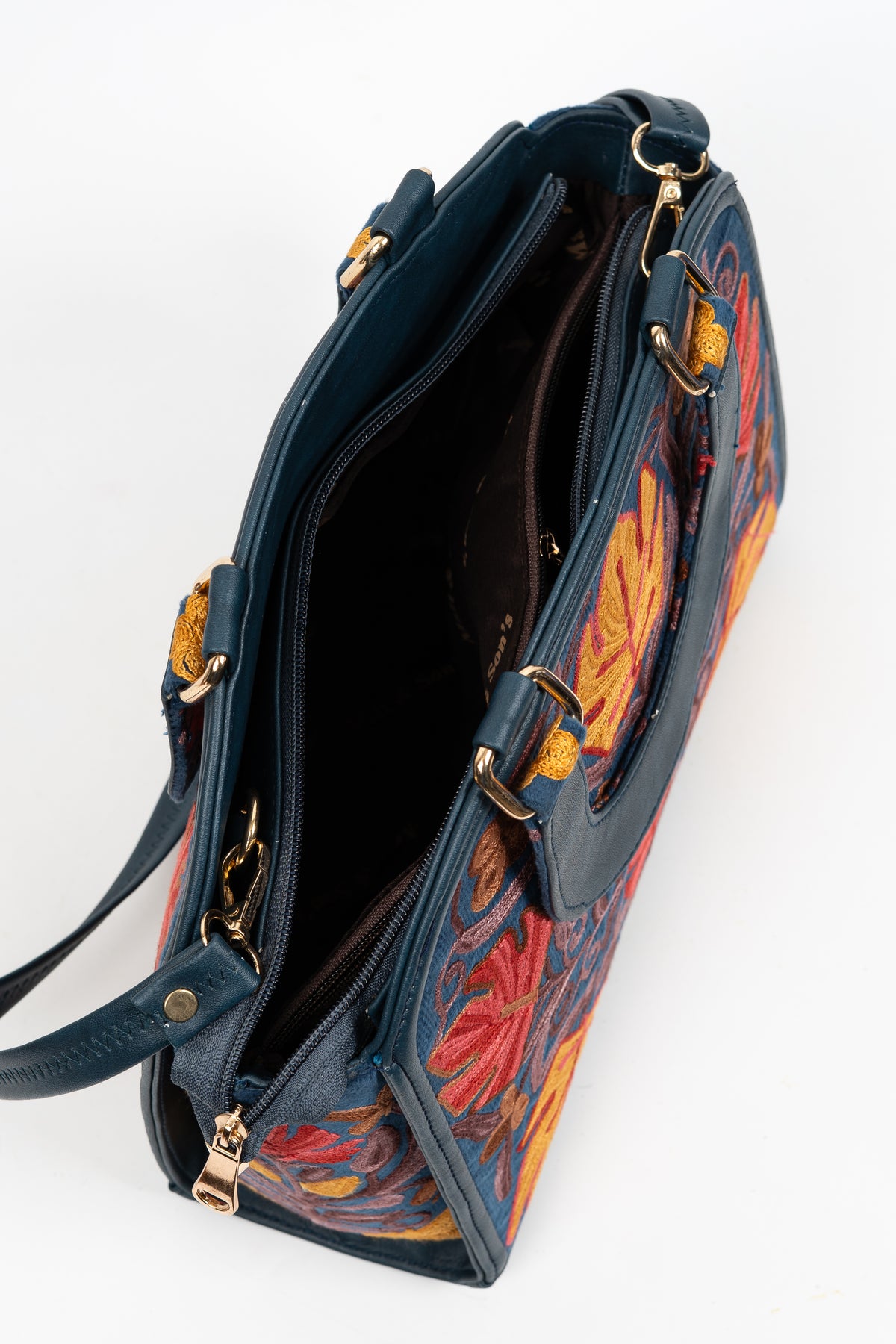 Top view into an open navy embroidered handbag showing its dark interior, zip closure and gold-toned strap clips