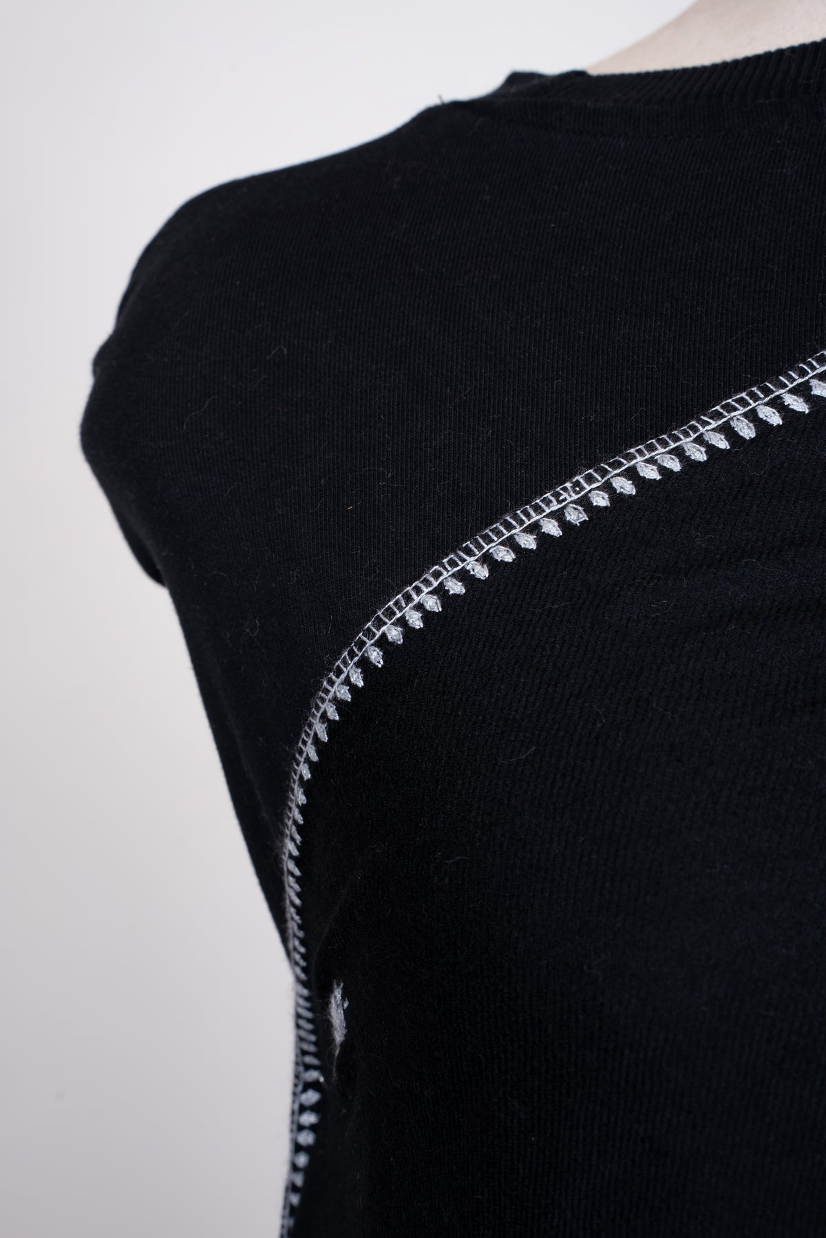 Close-up of a black scarf across a mannequin's chest, showing its narrow white embroidered leaf border.