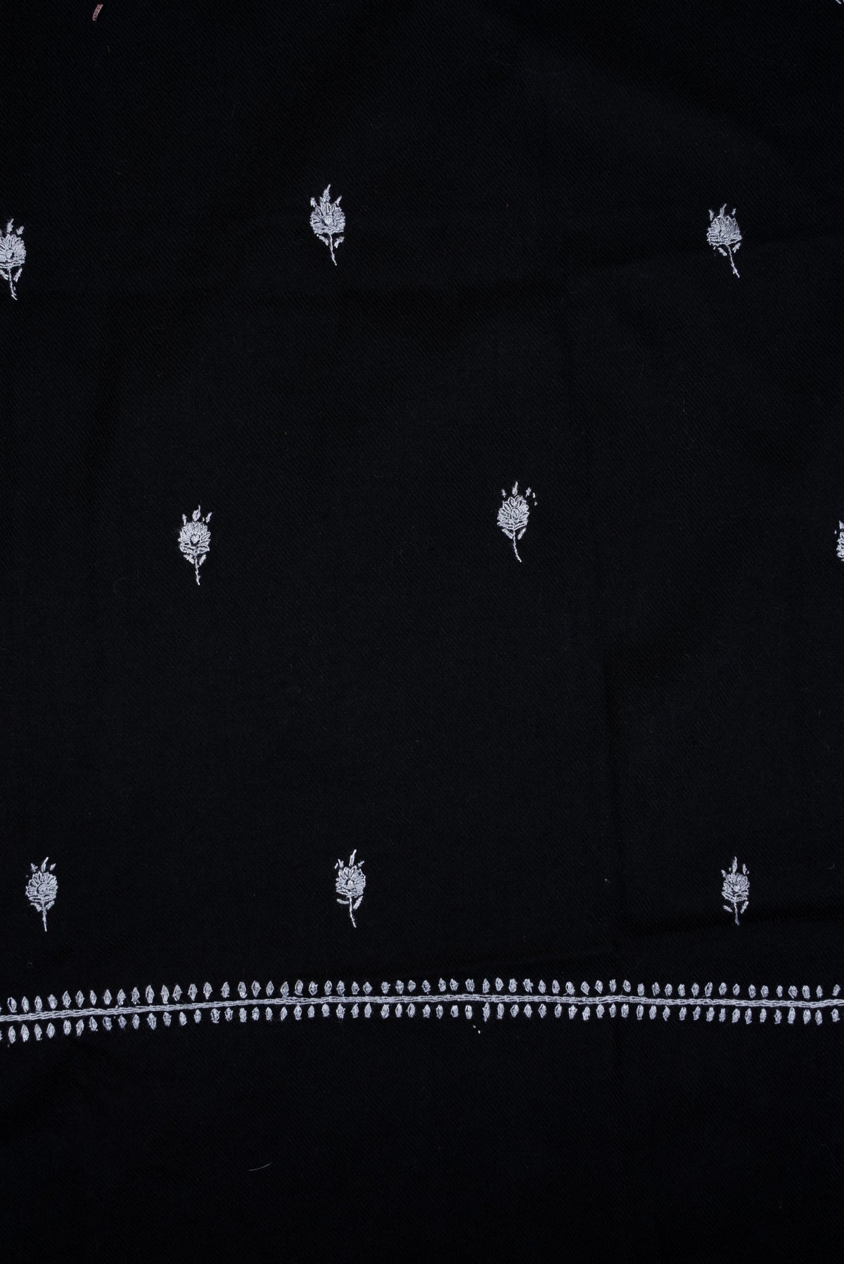 Flat detail of a black scarf, showing scattered small white embroidered flower sprigs above a narrow leafy end border.