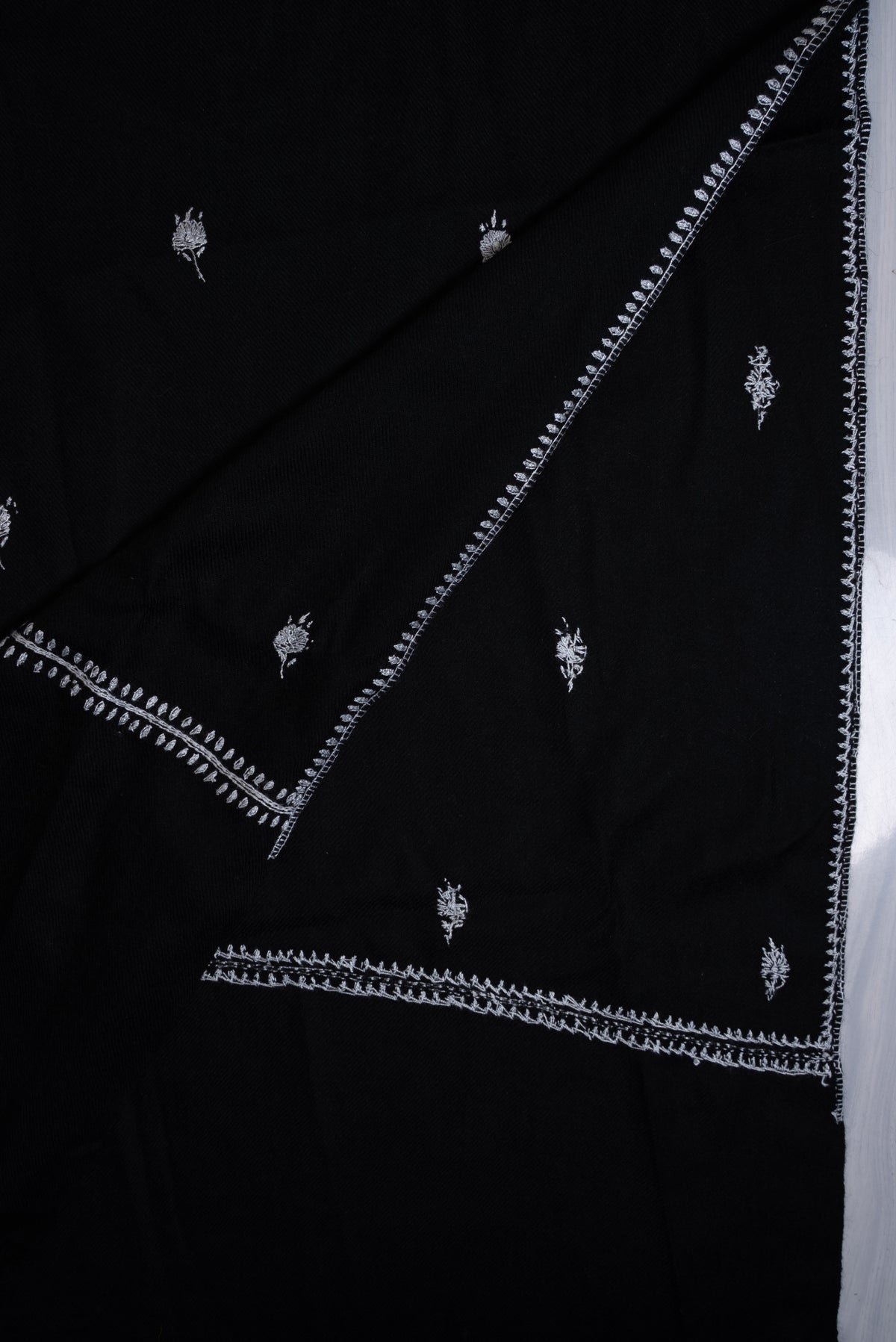 Black scarf folded diagonally, showing small white embroidered floral motifs and overlapping narrow white leafy borders.