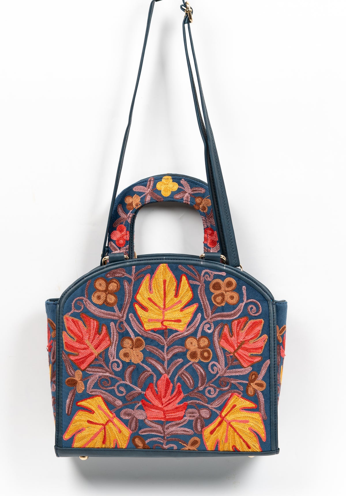 Navy Aari handbag hanging from a long shoulder strap, with red and yellow leaf motifs and an embroidered arched handle
