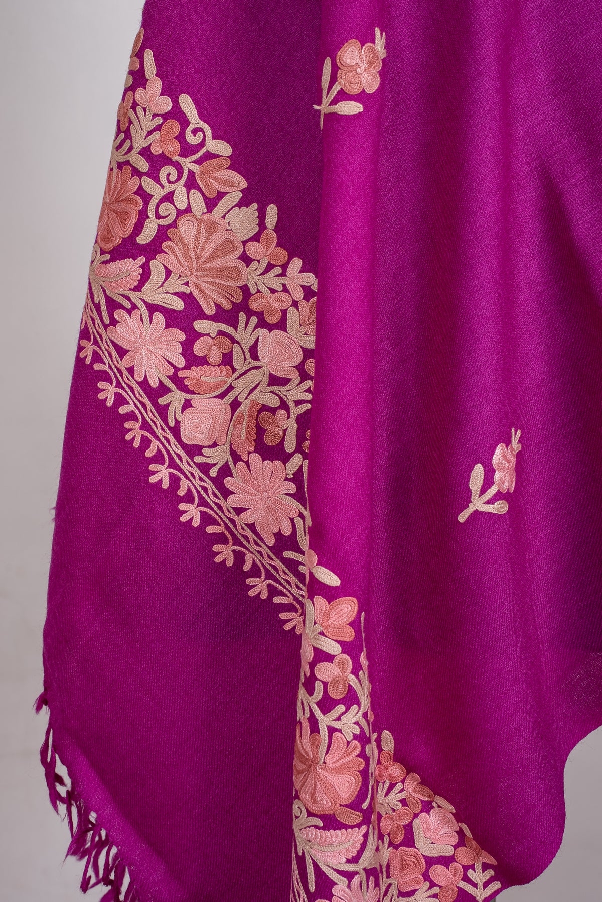 Lower draped detail of the magenta scarf, showing pale blush floral embroidery along the end border and matching fringe