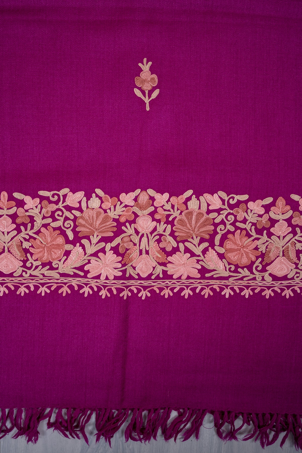 Detail of a small pale floral sprig above the magenta scarf’s blush-and-beige embroidered end border