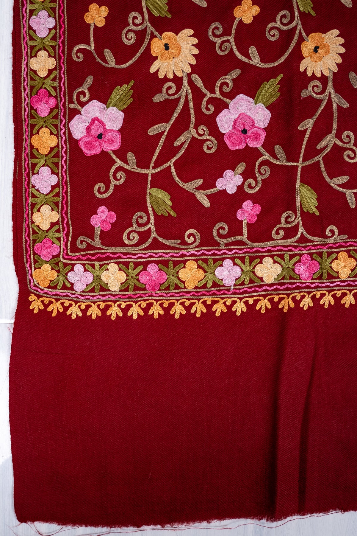 Corner detail of maroon shawl showing pink and golden Aari flowers, a narrow floral border and plain maroon end