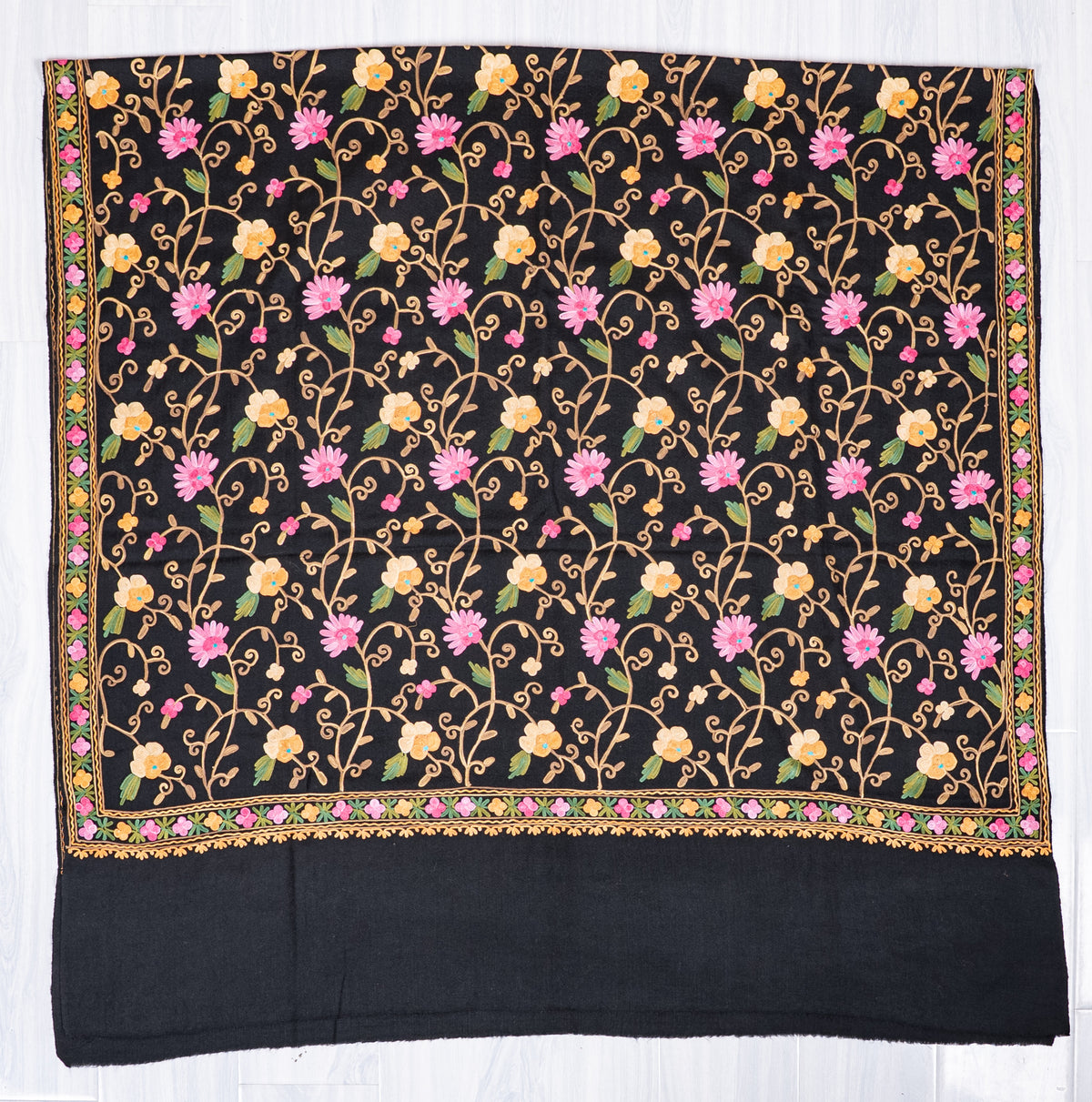 Black shawl laid flat, with pink and cream Aari floral vines covering a bordered panel above a wide plain black end.