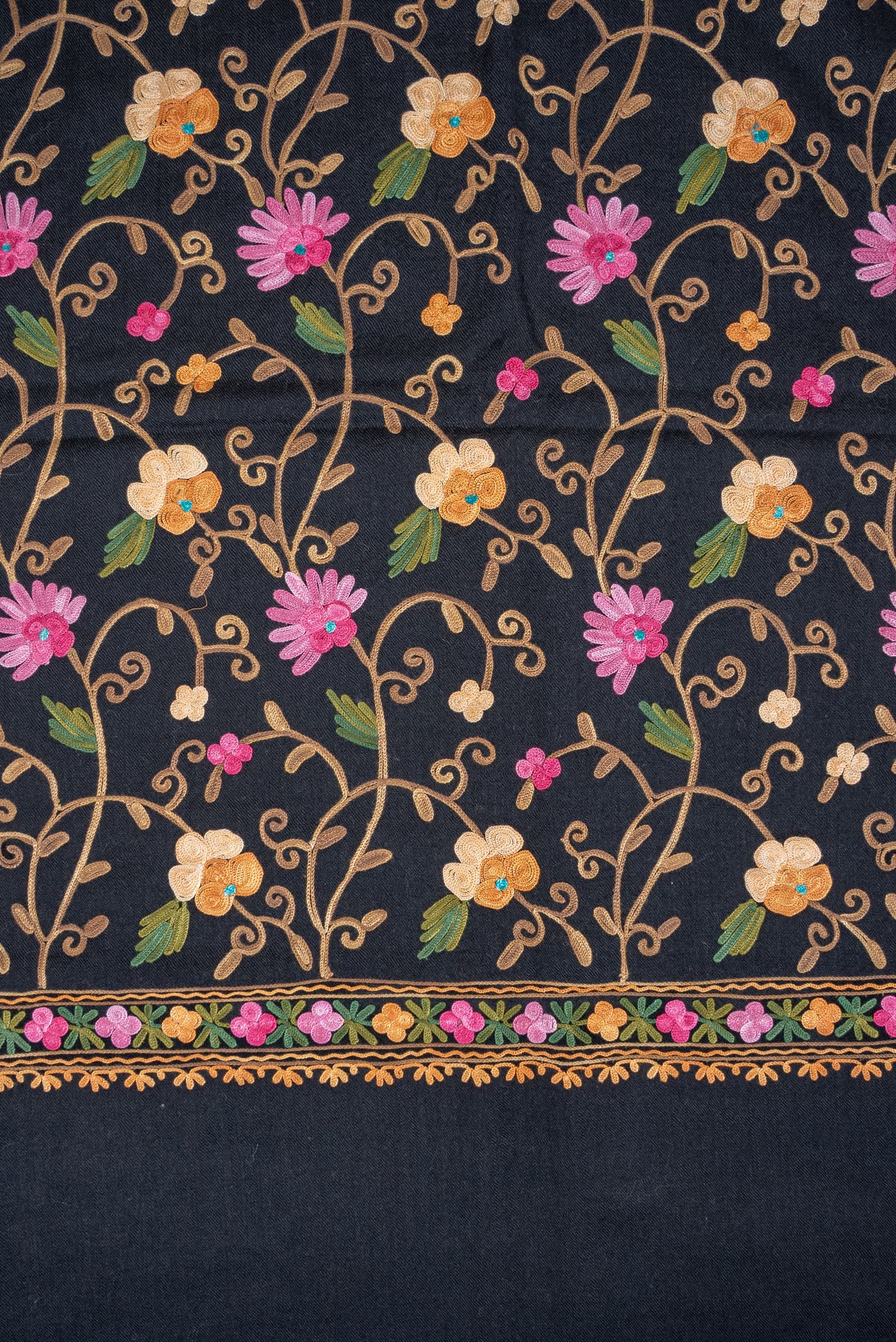 Flat detail of a black shawl's pink and cream Aari floral vines, with a narrow flower border above the plain black end.