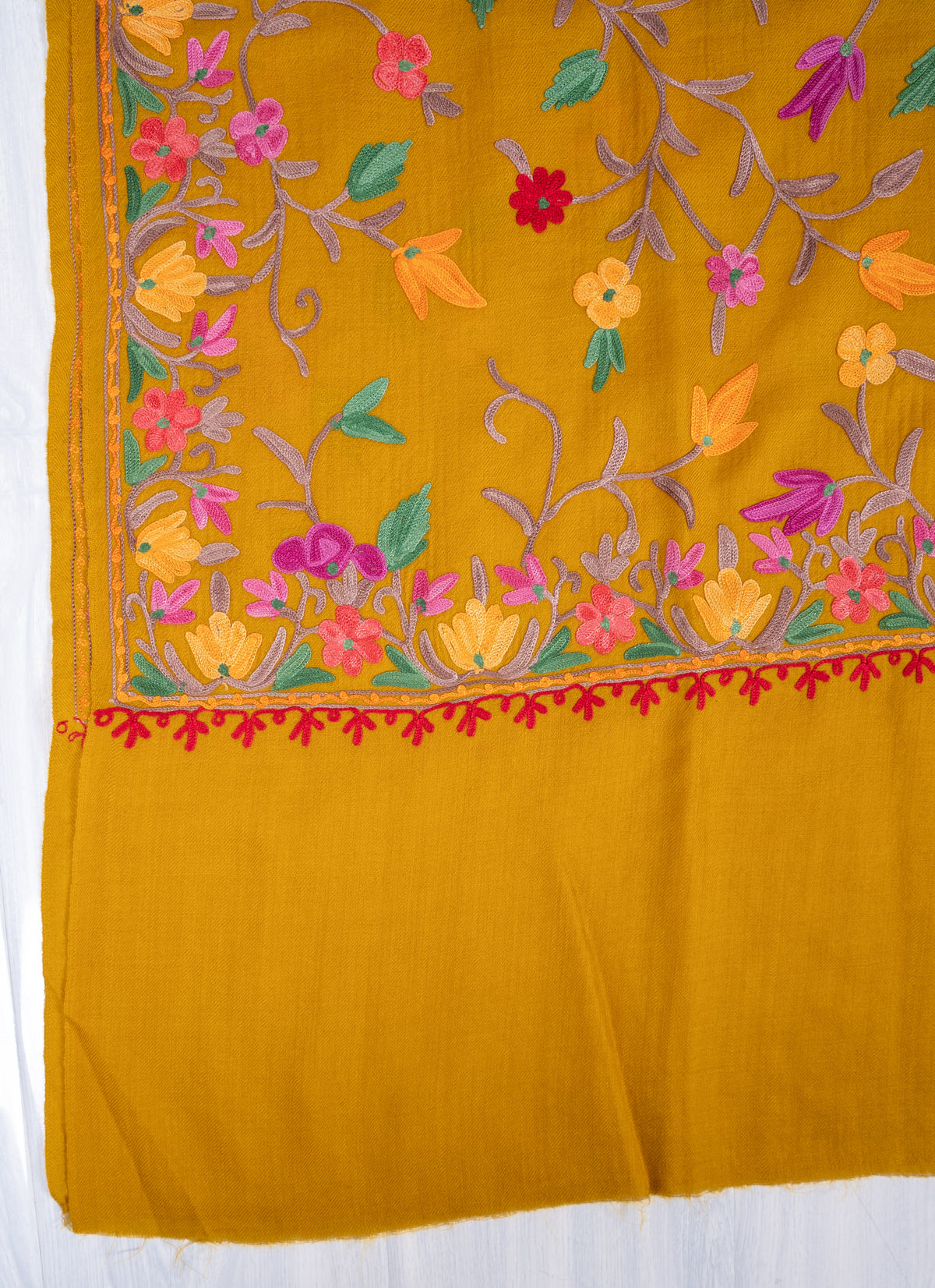 Corner detail of mustard shawl showing colourful floral embroidery, matching borders and the plain mustard end